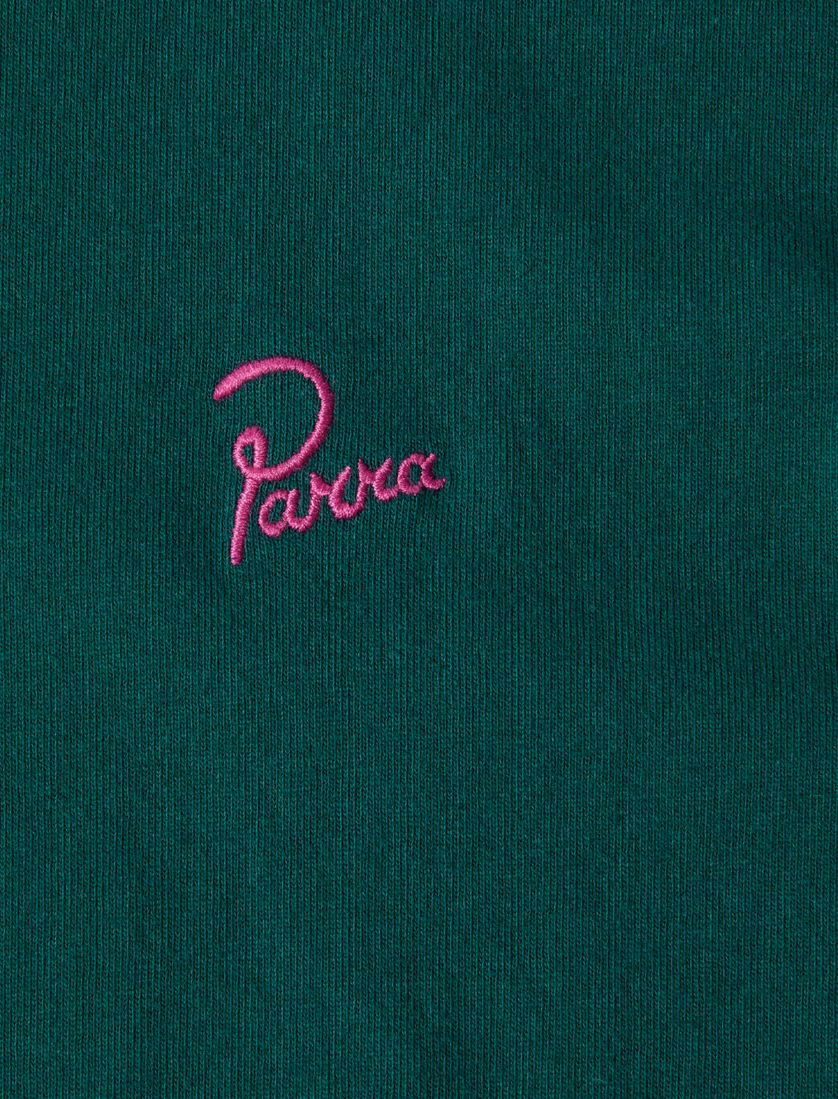 Close-up of a green fabric with pink embroidered by parra logo on a dark green background