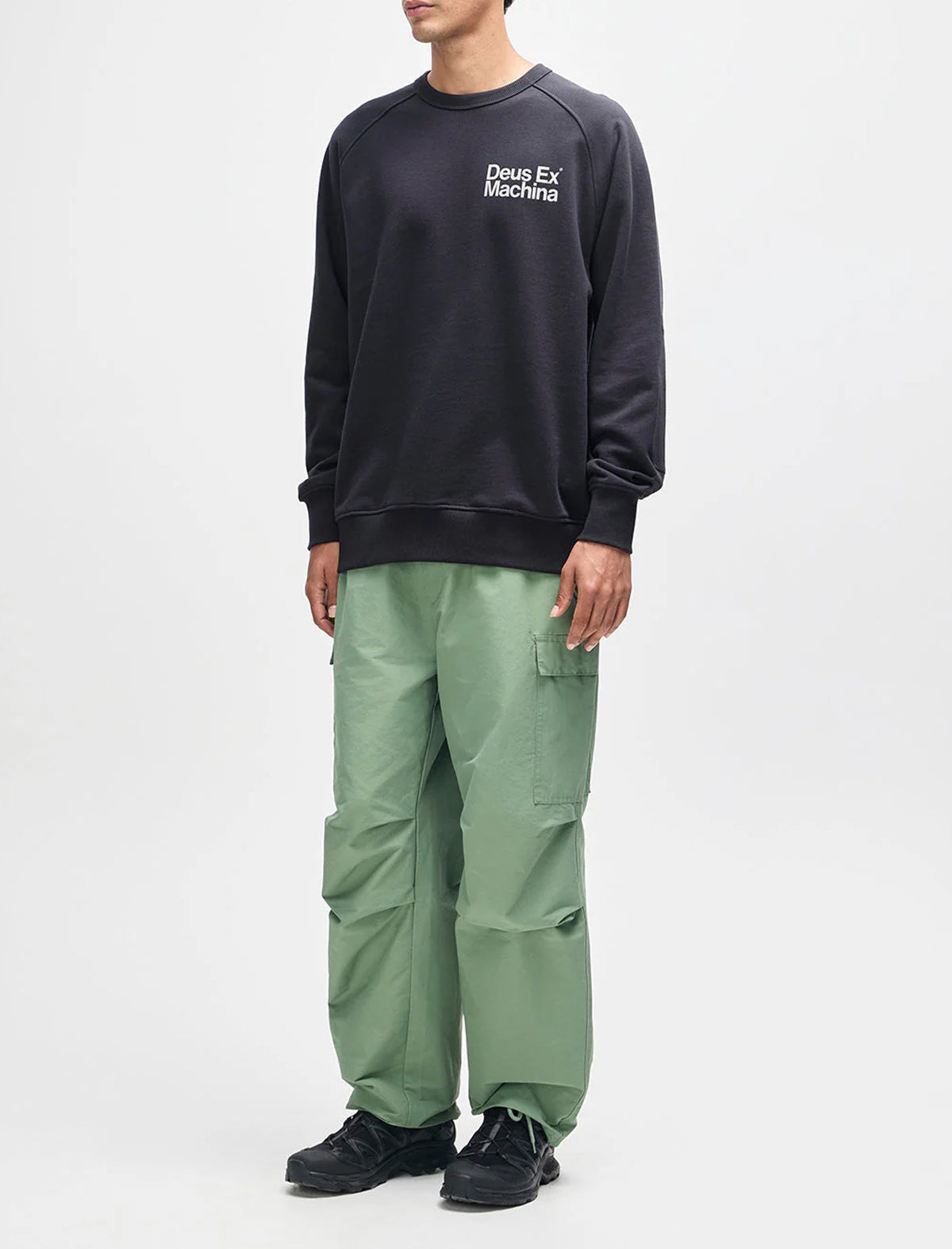 Person wearing a black sweatshirt and green pants on a white background