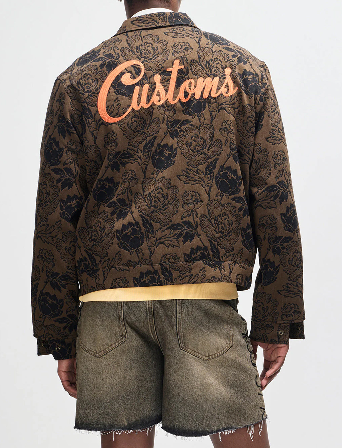 Person wearing a patterned jacket with 'Customs' text on the back, standing against a white background.