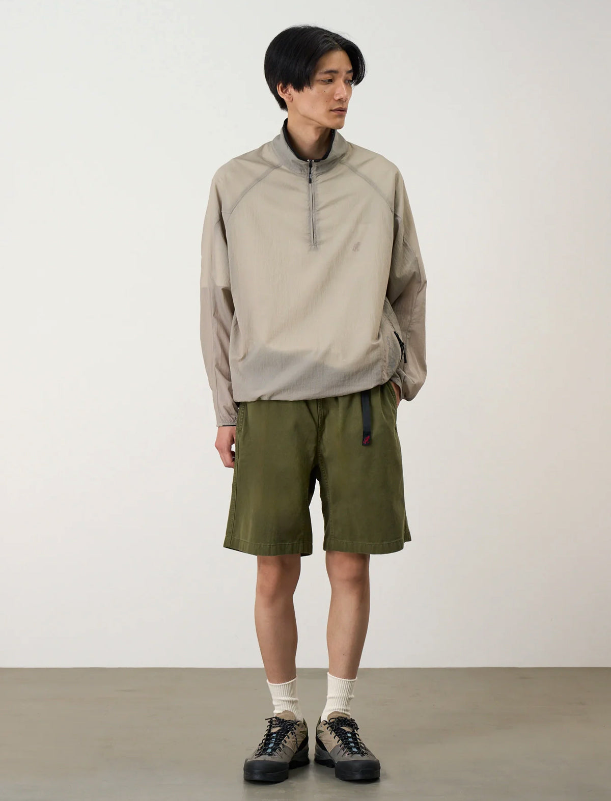 Person wearing a beige jacket and green shorts against a white background