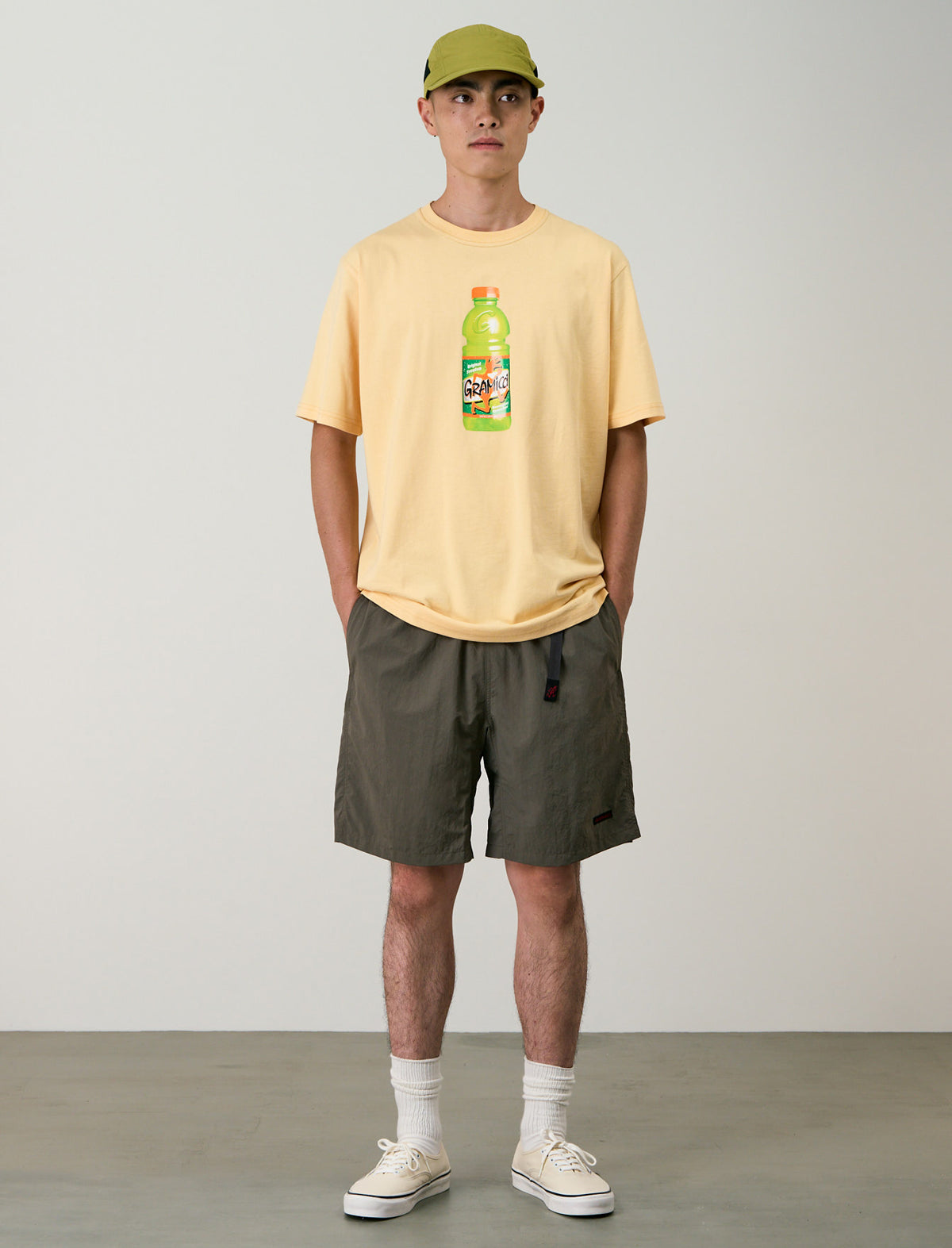 Person wearing a yellow t-shirt with a bottle graphic and green shorts on a plain background