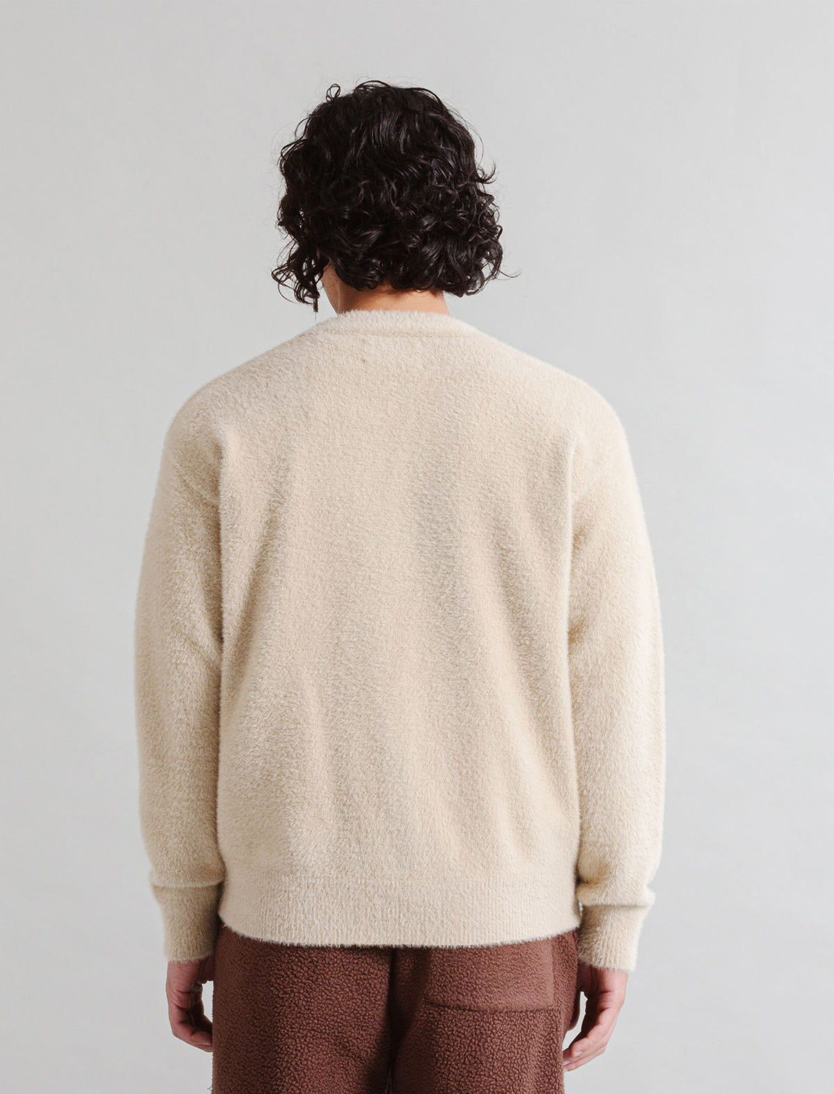 Person wearing a beige sweater and brown pants against a light gray background