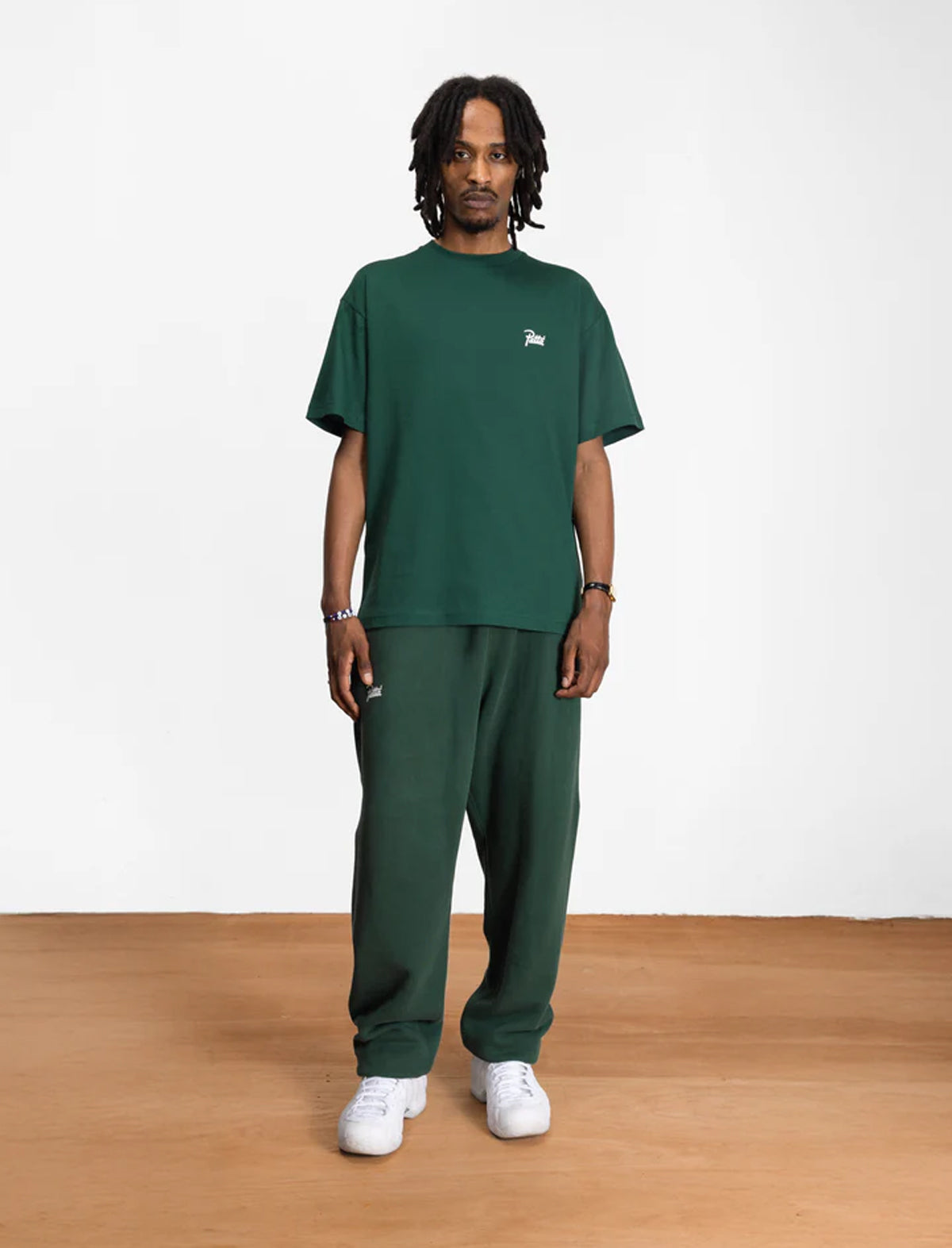 Person wearing a green t-shirt and pants with a small logo on a white background