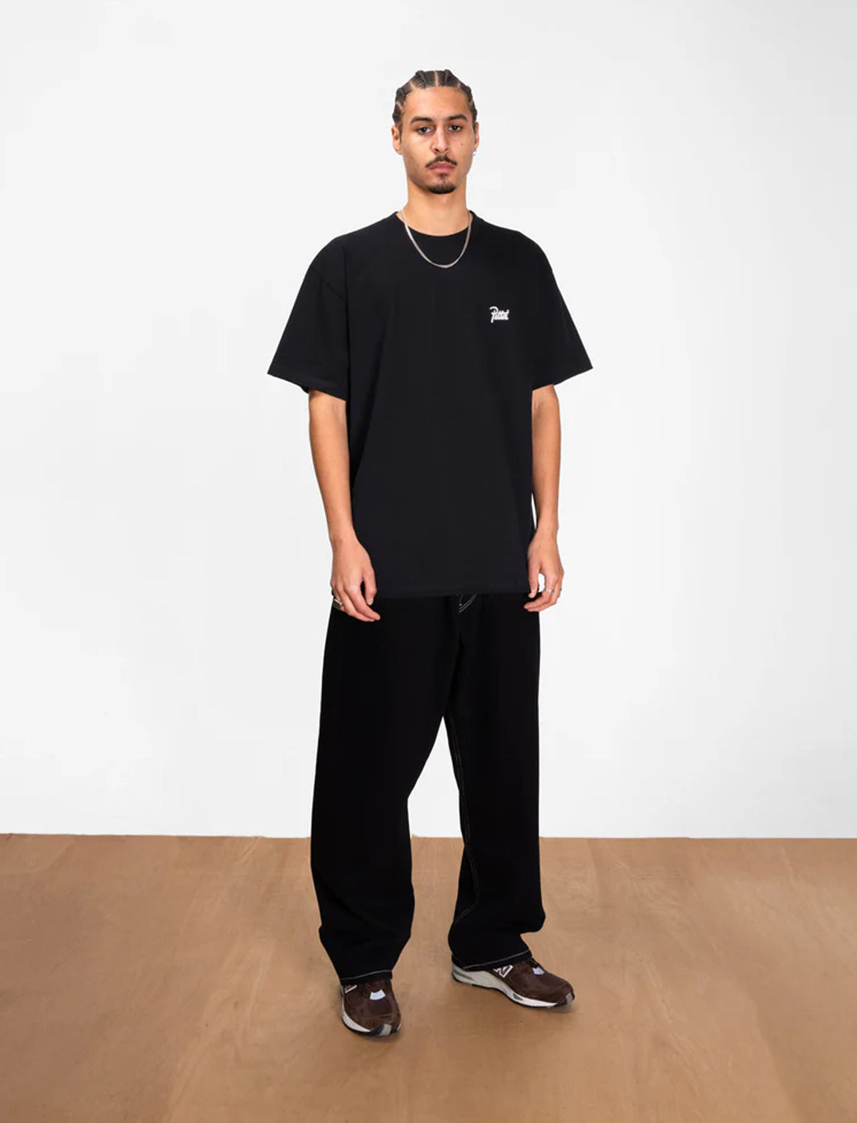Person wearing a black Patta t-shirt and pants standing against a white wall.