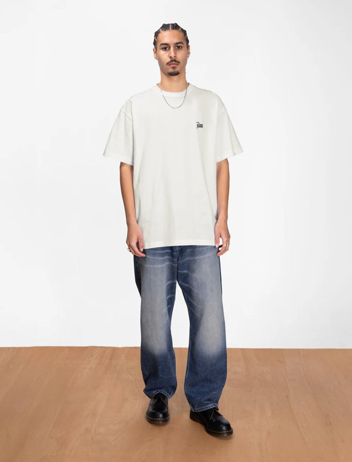 Person wearing a Patta white t-shirt and blue jeans standing against a plain white background