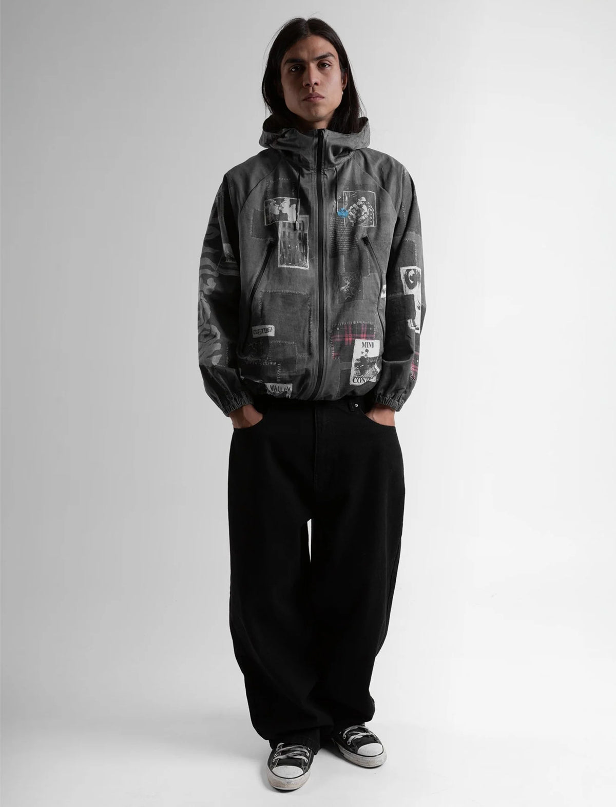 Person wearing a gray hooded jacket with patches on a white background