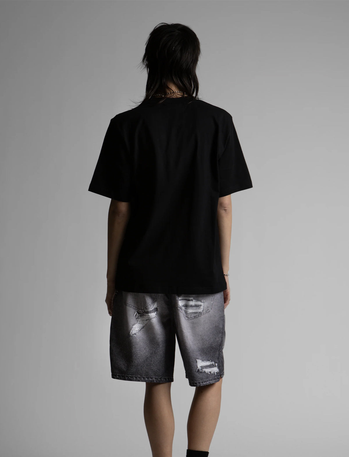 Person wearing a black t-shirt and distressed gray shorts on a plain background