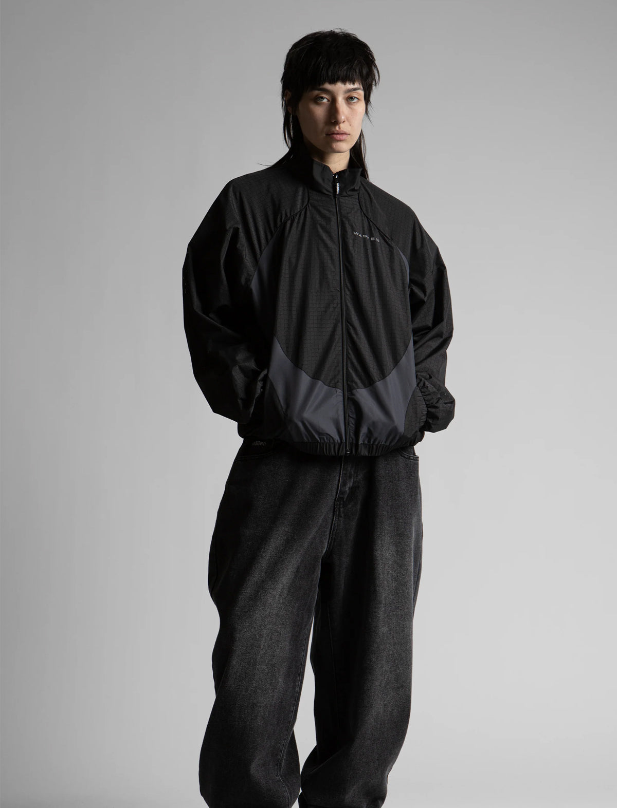Person wearing a black jacket and pants on a gray background