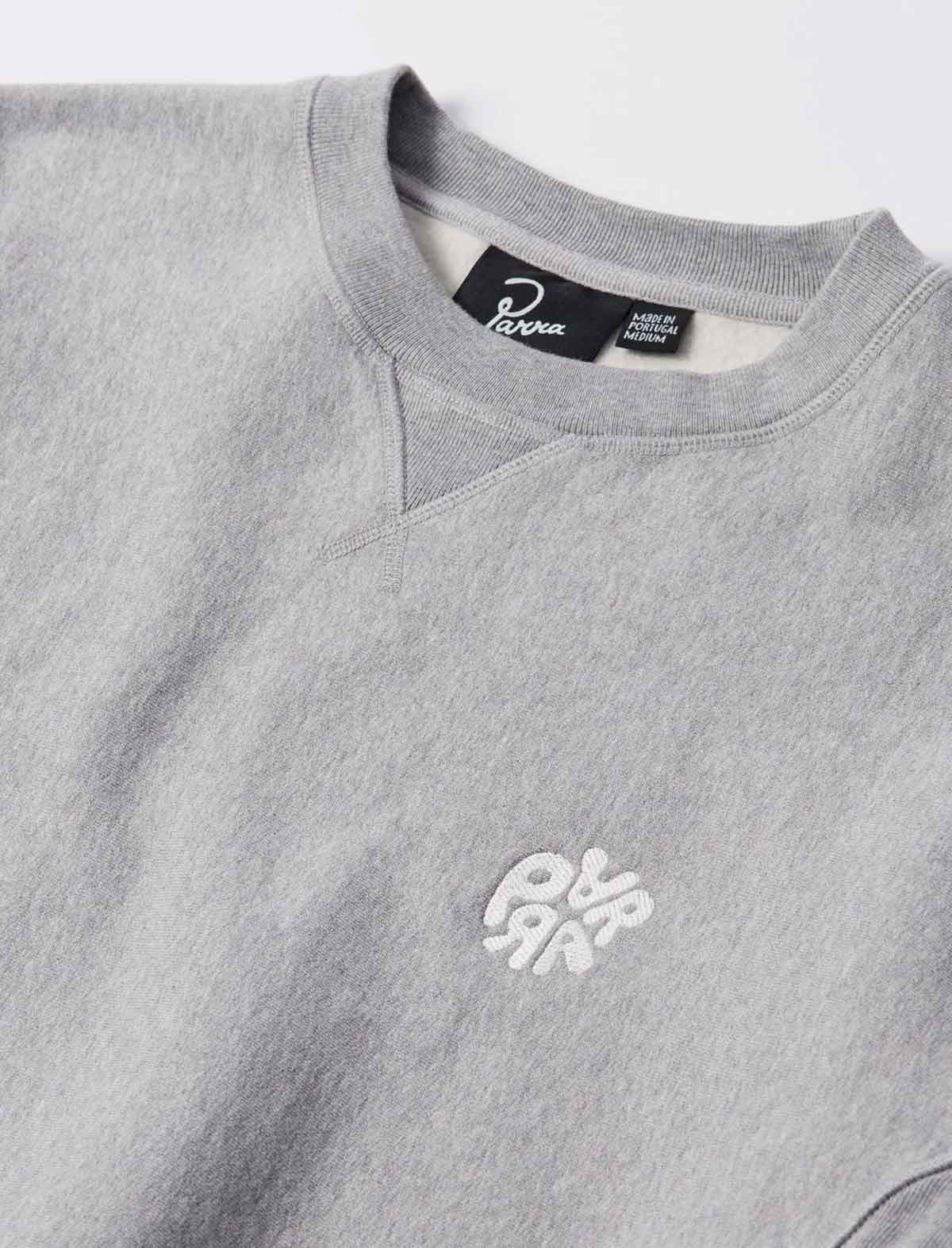 Close-up of a light gray crewneck sweatshirt with a white embroidered logo on the chest and a black neck label.