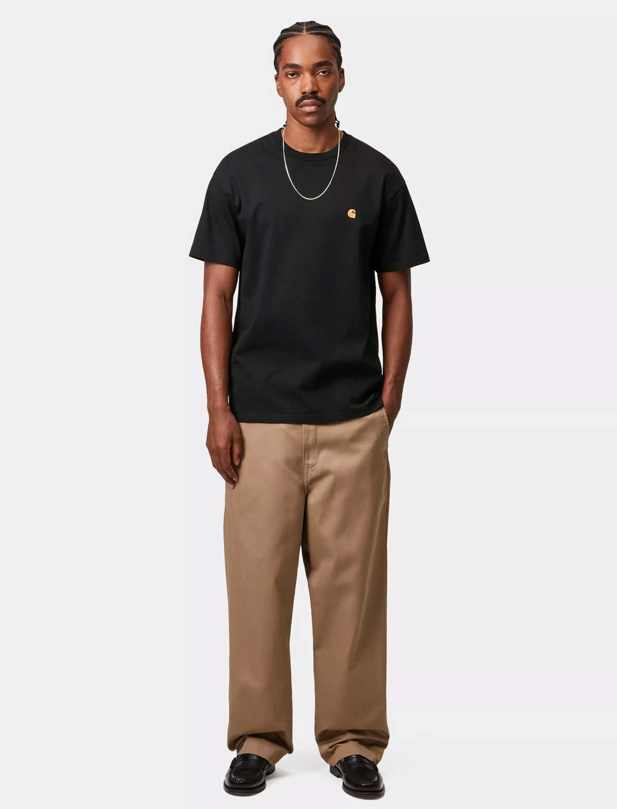 Man wearing a Carhartt WIP S/S Chase black t-shirt with a logo and beige pants on a white background