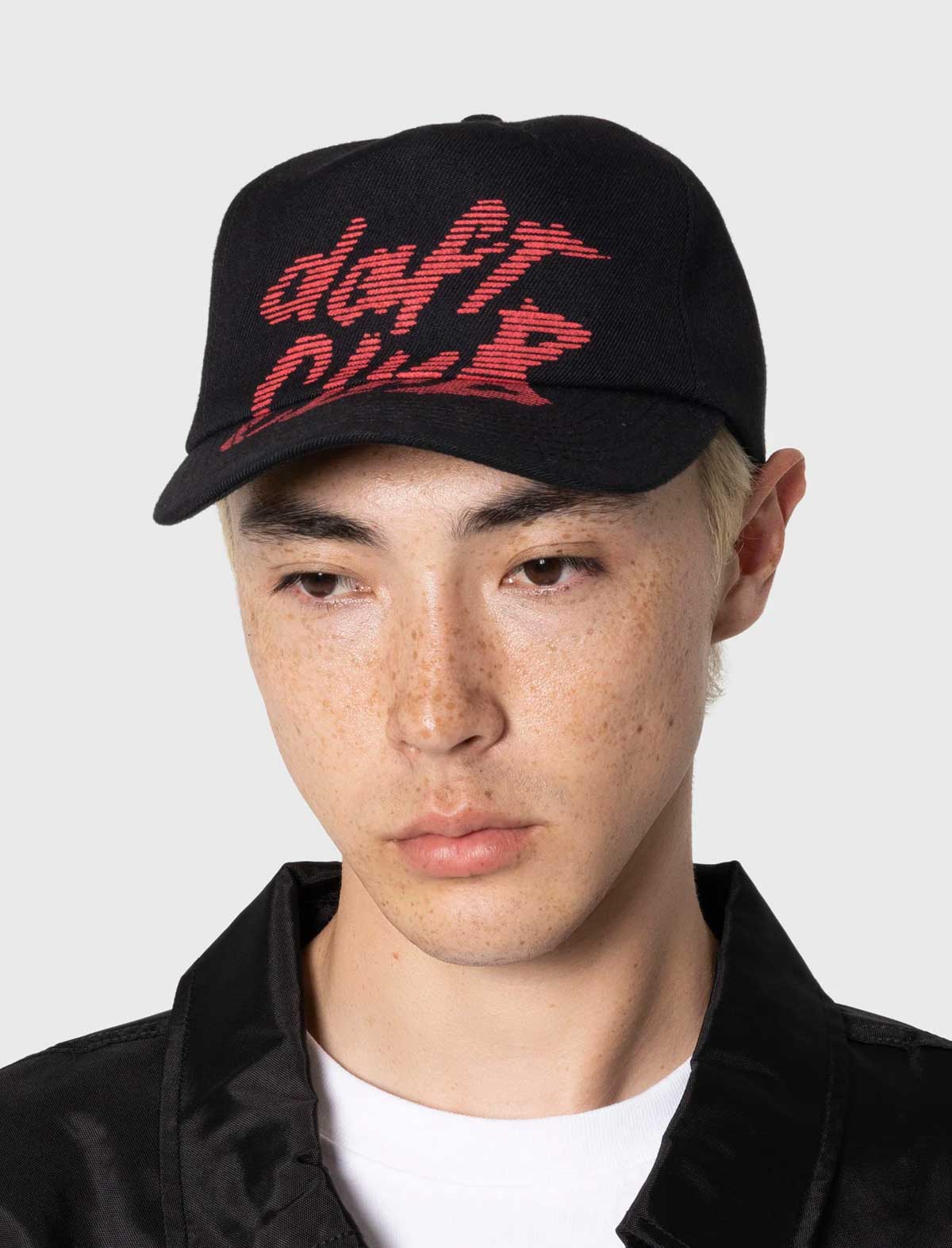 Person wearing a Pleasures x Daft Punk black cap with red text on a white background