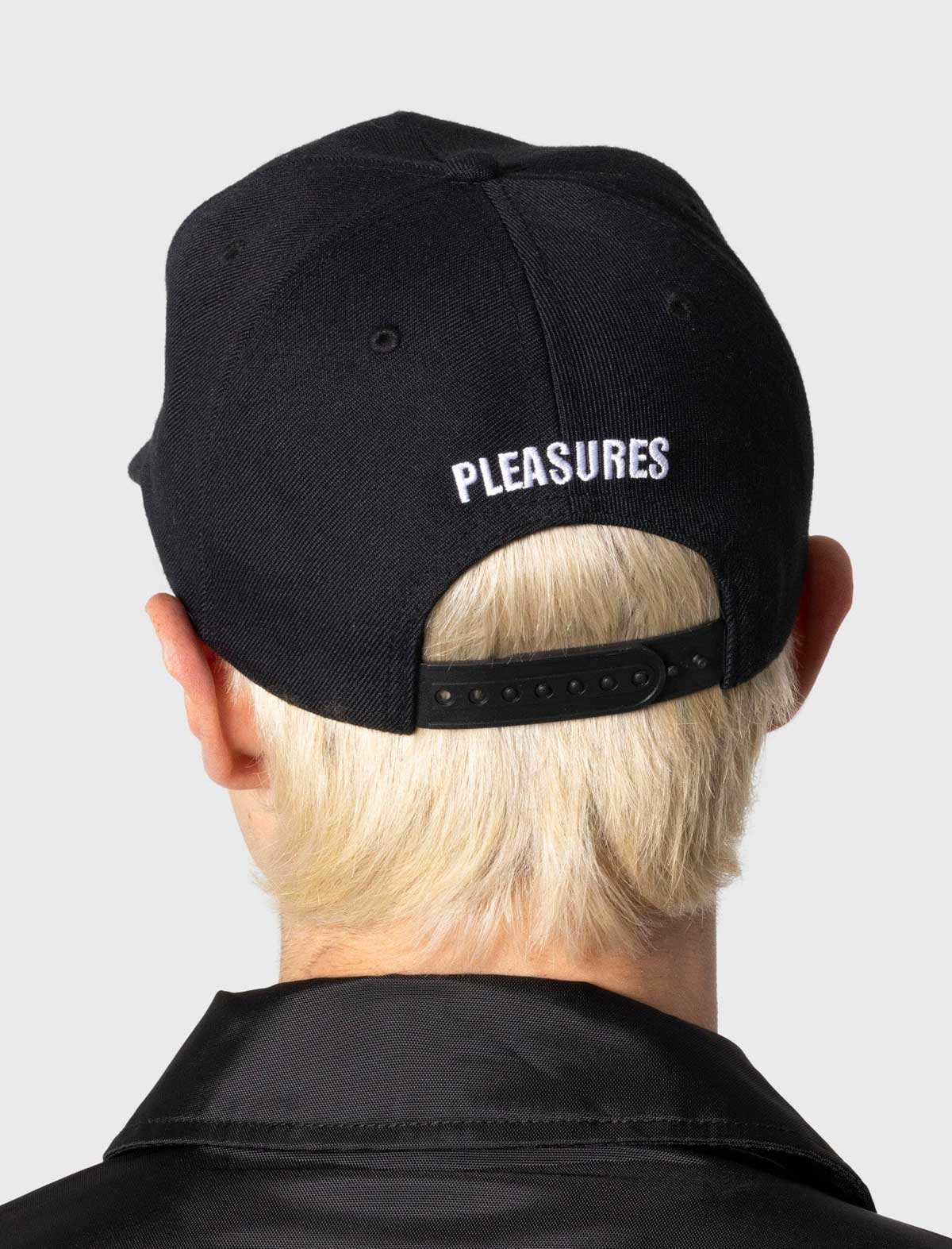 Person wearing a black cap with 'PLEASURES' branding on the back, against a plain background.