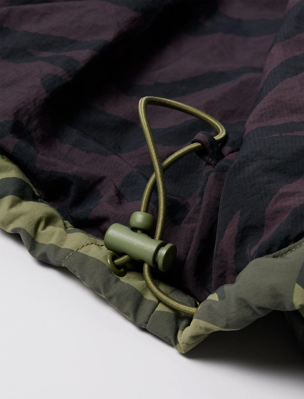 Close-up of a camouflage-patterned sleeping bag with a green drawstring on a white background