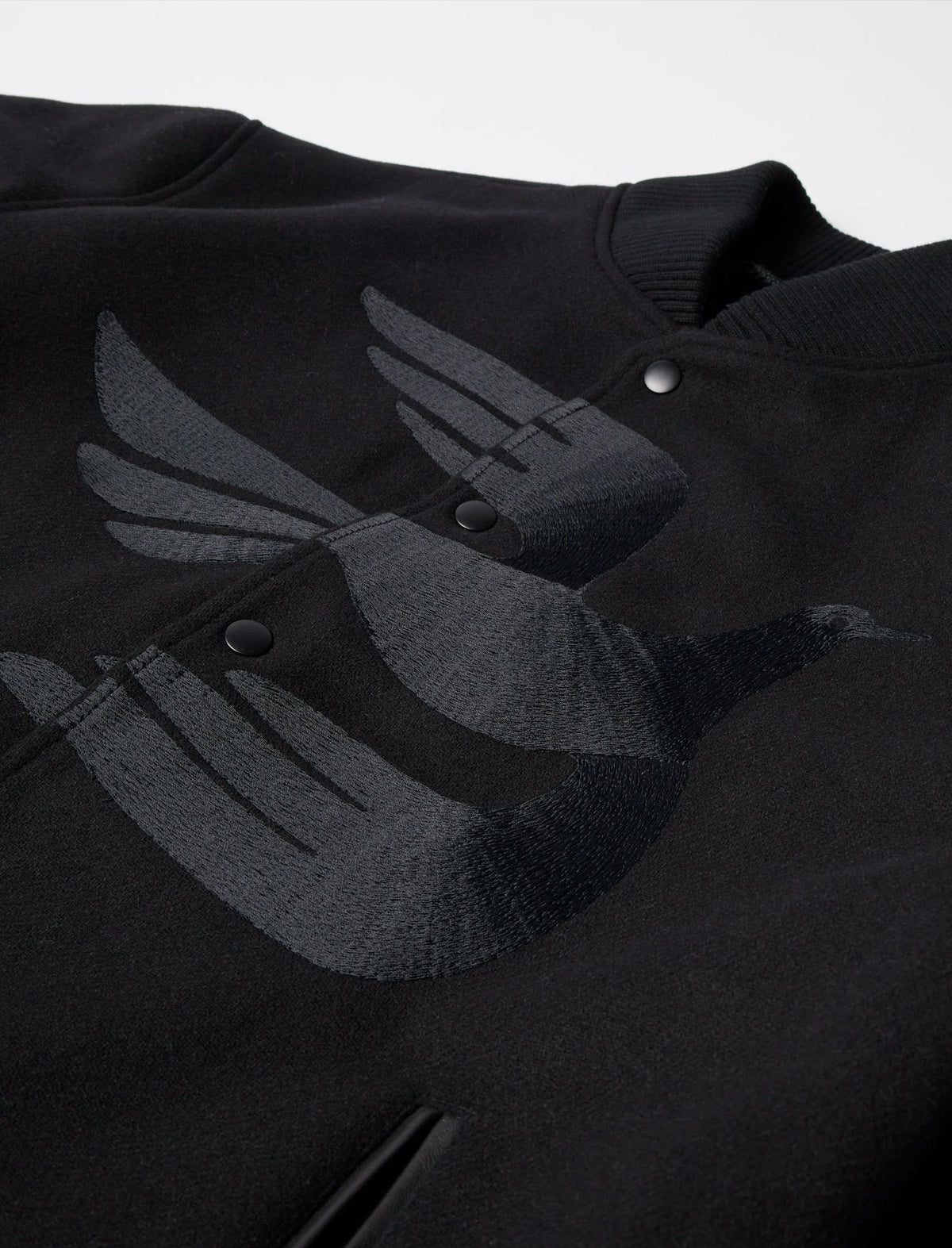 Black varsity jacket with a winged logo on a white background