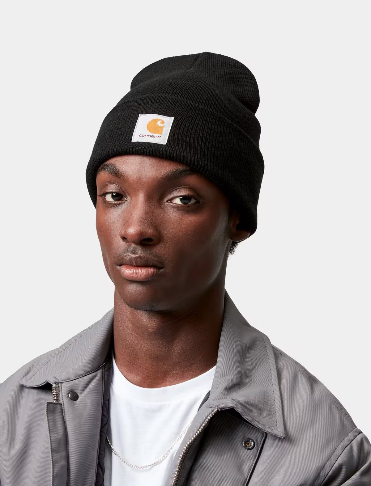 Person wearing a black carhartt wip beanie with a brand logo on a light gray background