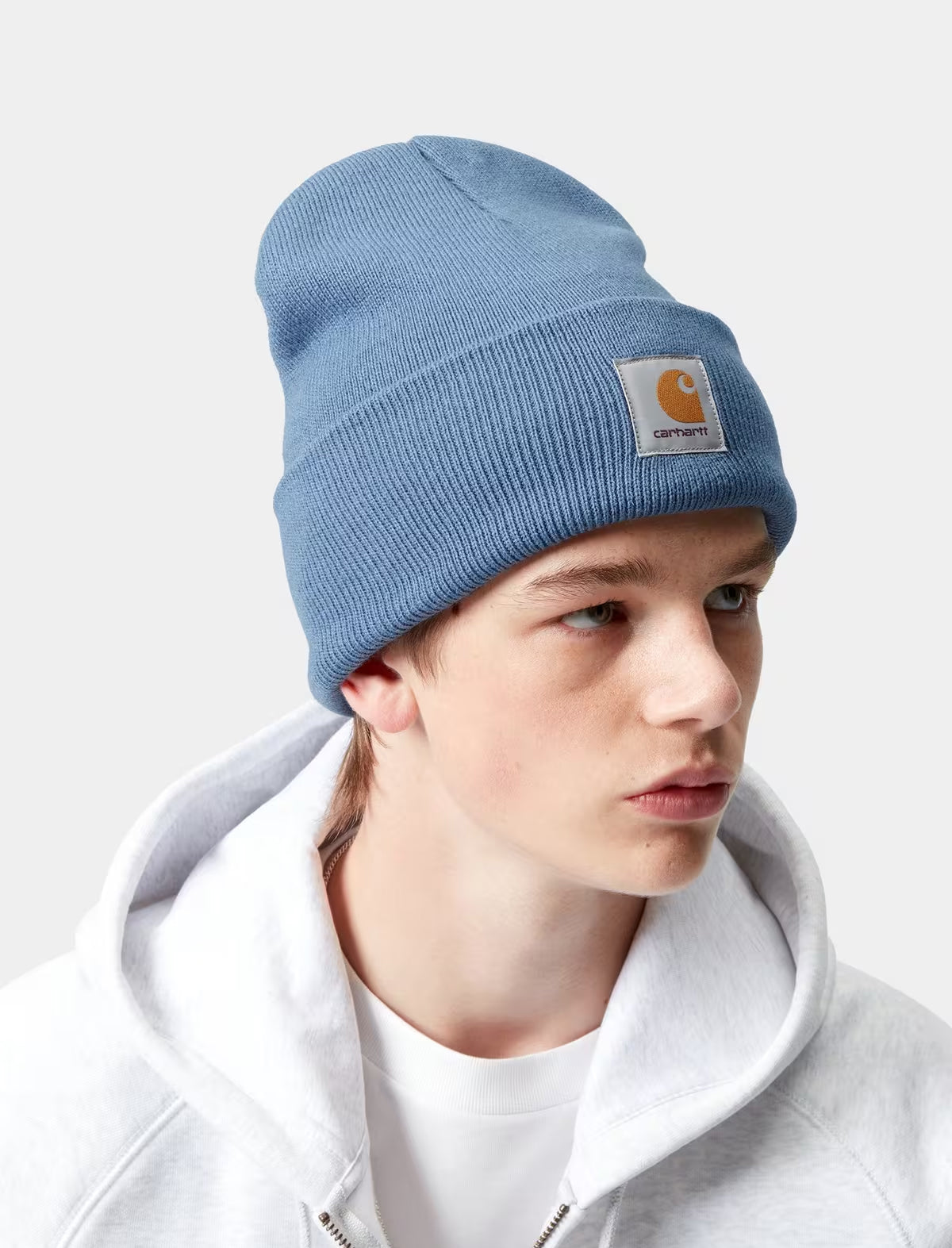 Person wearing a Carhartt WIP blue beanie with a brand logo on a white background