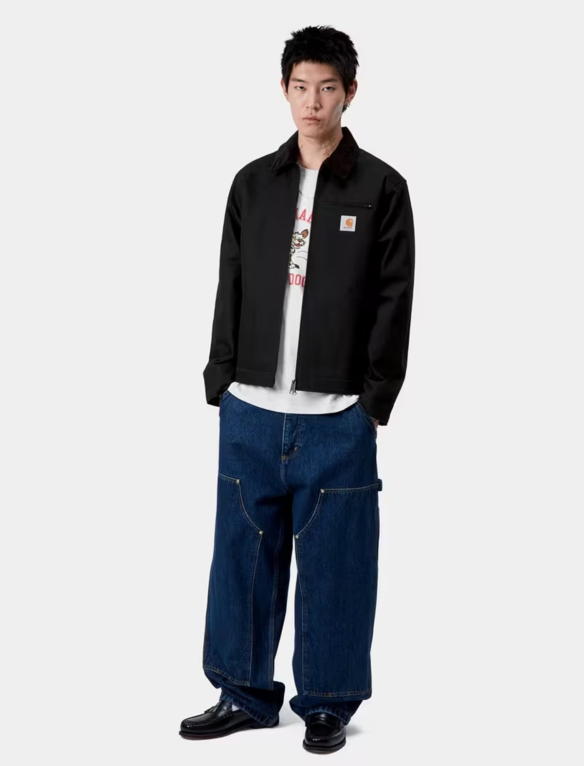 Person wearing a carhartt detroit black jacket and blue jeans on a white background