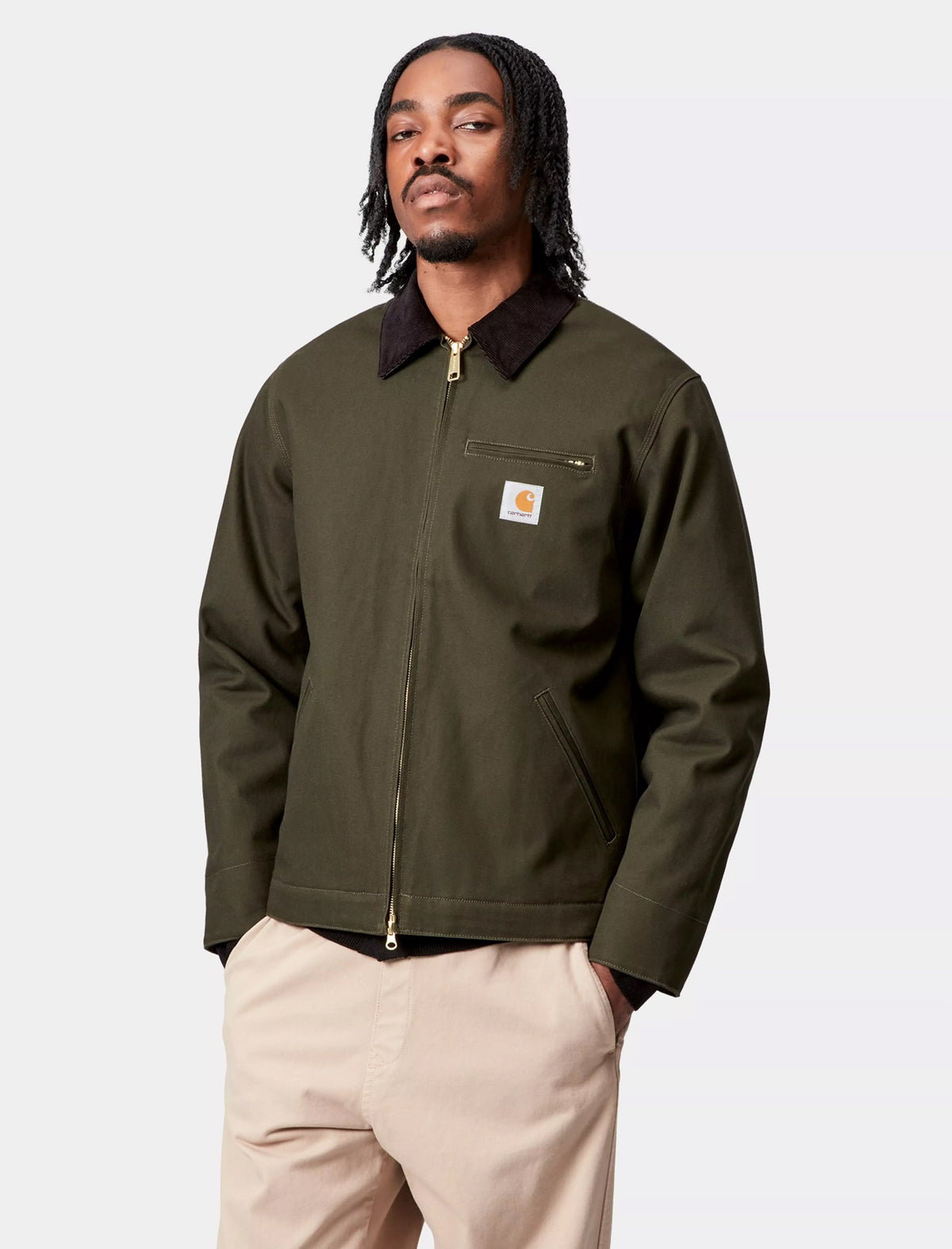 Man wearing a Carhartt WIP Detroit green jacket with a visible brand logo on a light gray background