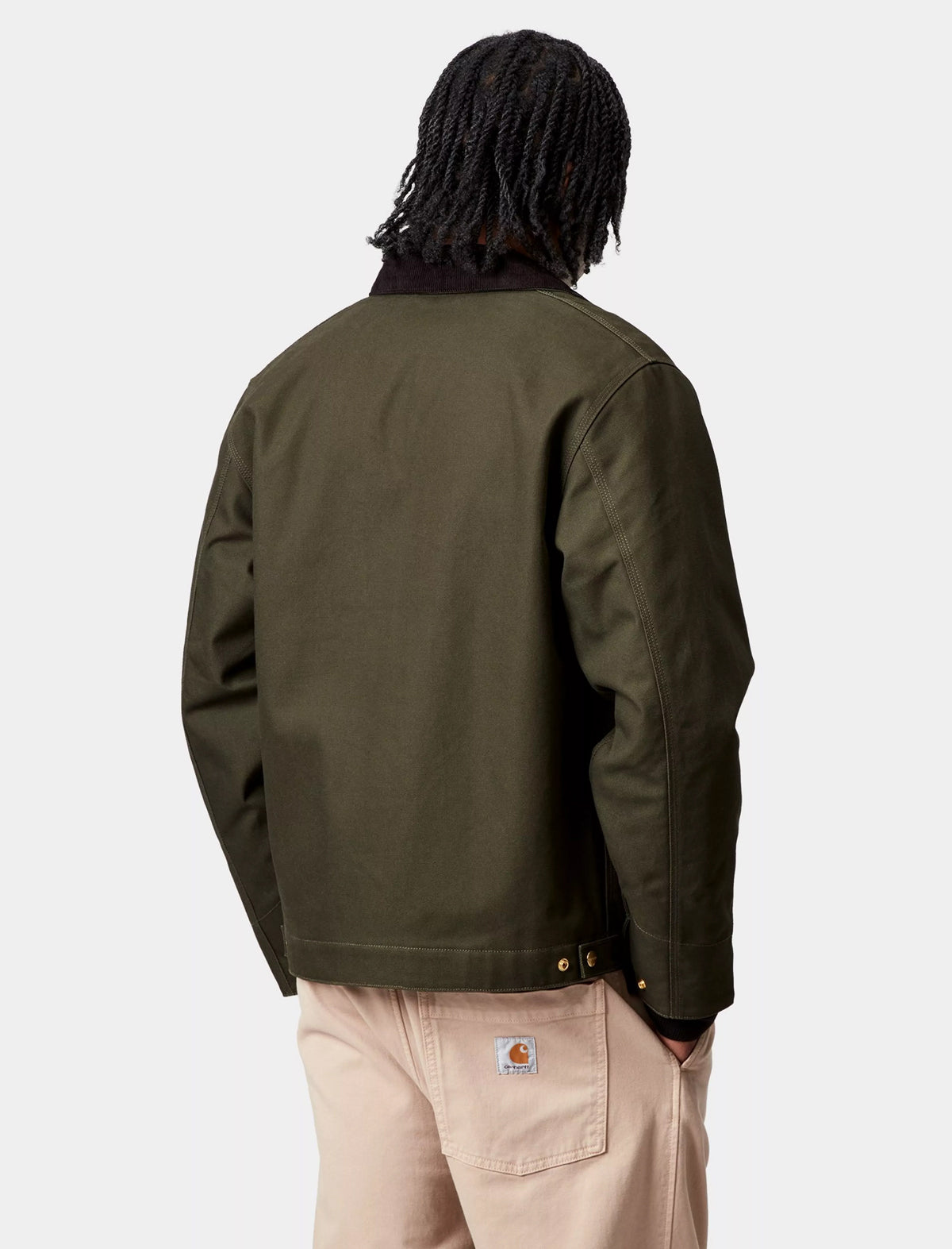Person wearing a Carhartt WIP Detroit green jacket and beige pants on a white background