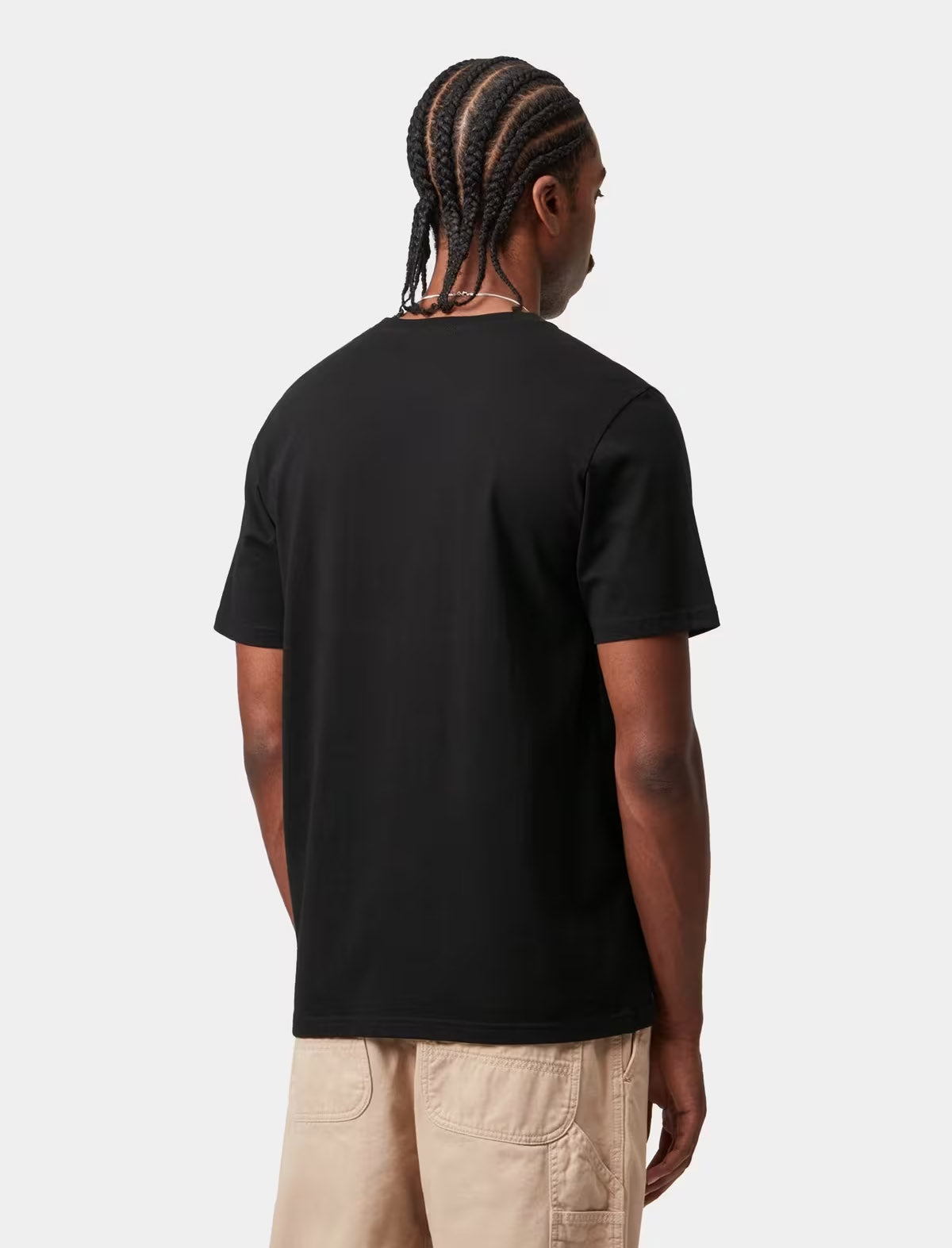 A man with braided hair is shown from the back wearing a solid black short-sleeve t-shirt and beige cargo shorts against a light gray studio background.