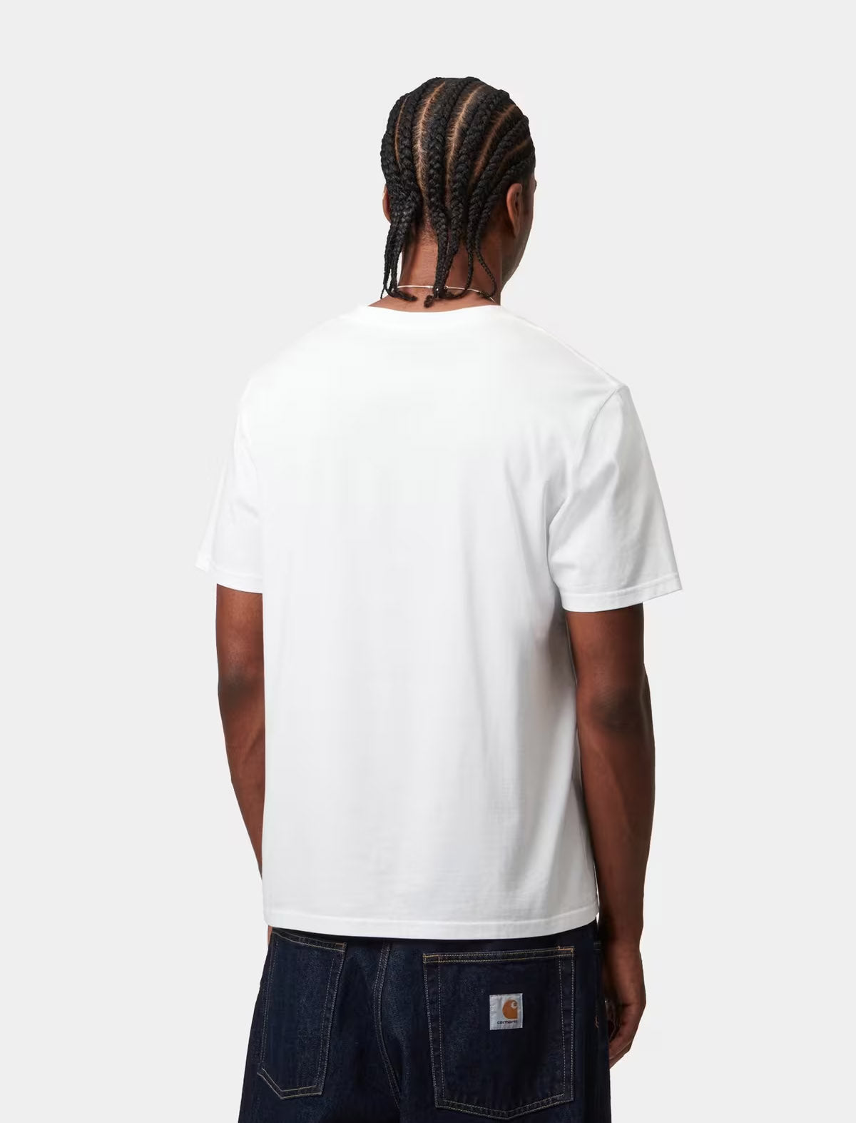 A man viewed from behind wearing a plain white short-sleeve t-shirt and dark blue jeans with a visible Carhartt logo patch on the back pocket, set against a solid light gray background.