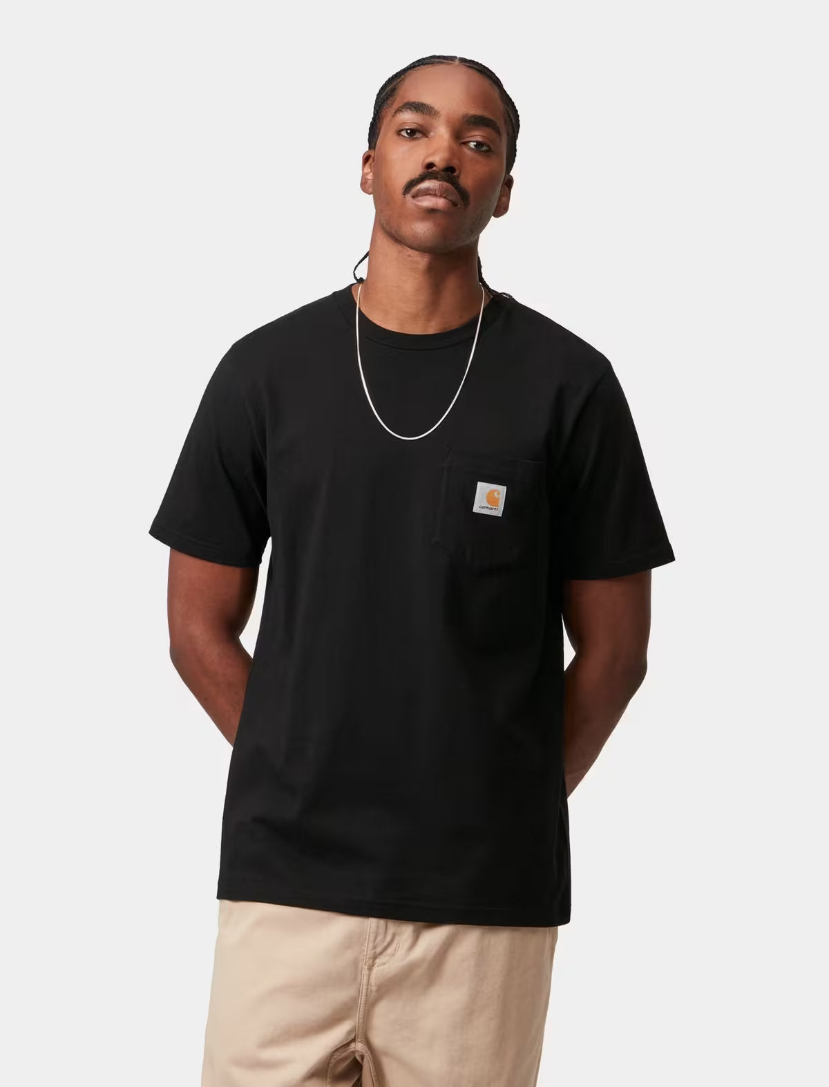 A man wearing a black Carhartt pocket t-shirt and beige pants, standing against a light gray background.