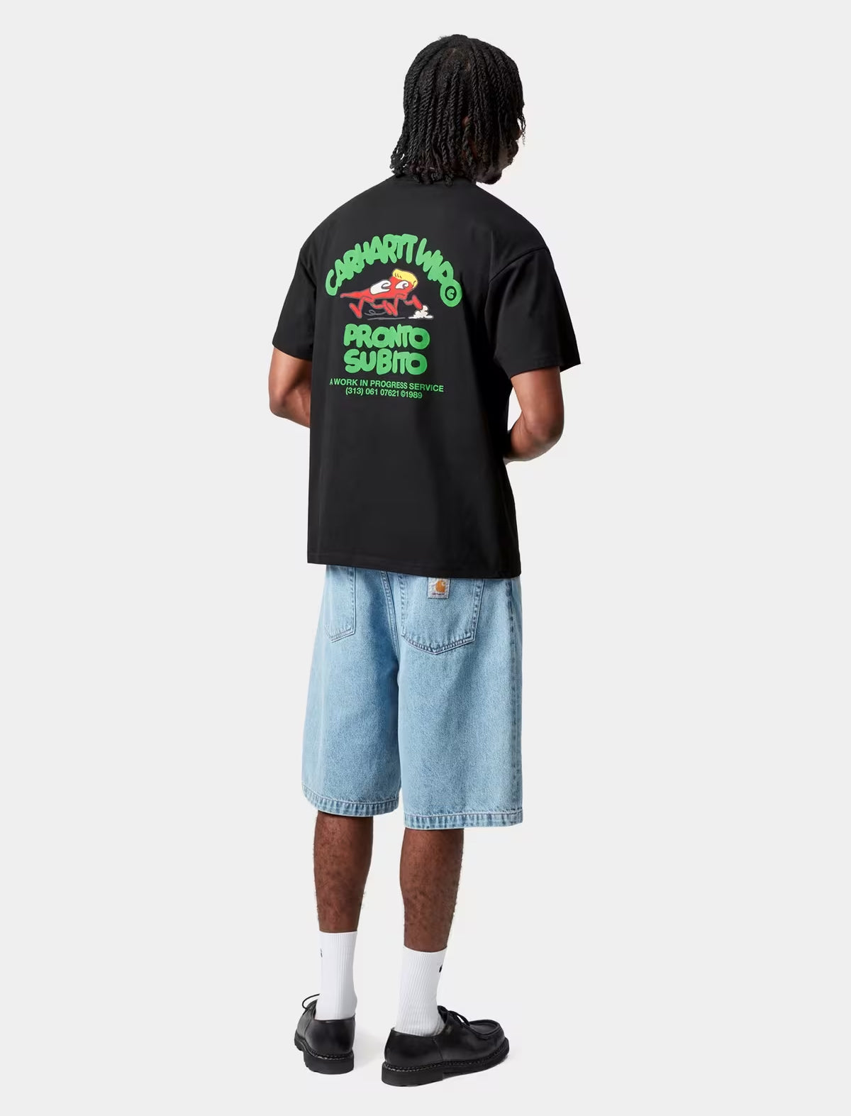 Person wearing a carhartt wip black t-shirt with green text and graphics on the back, standing against a white background.