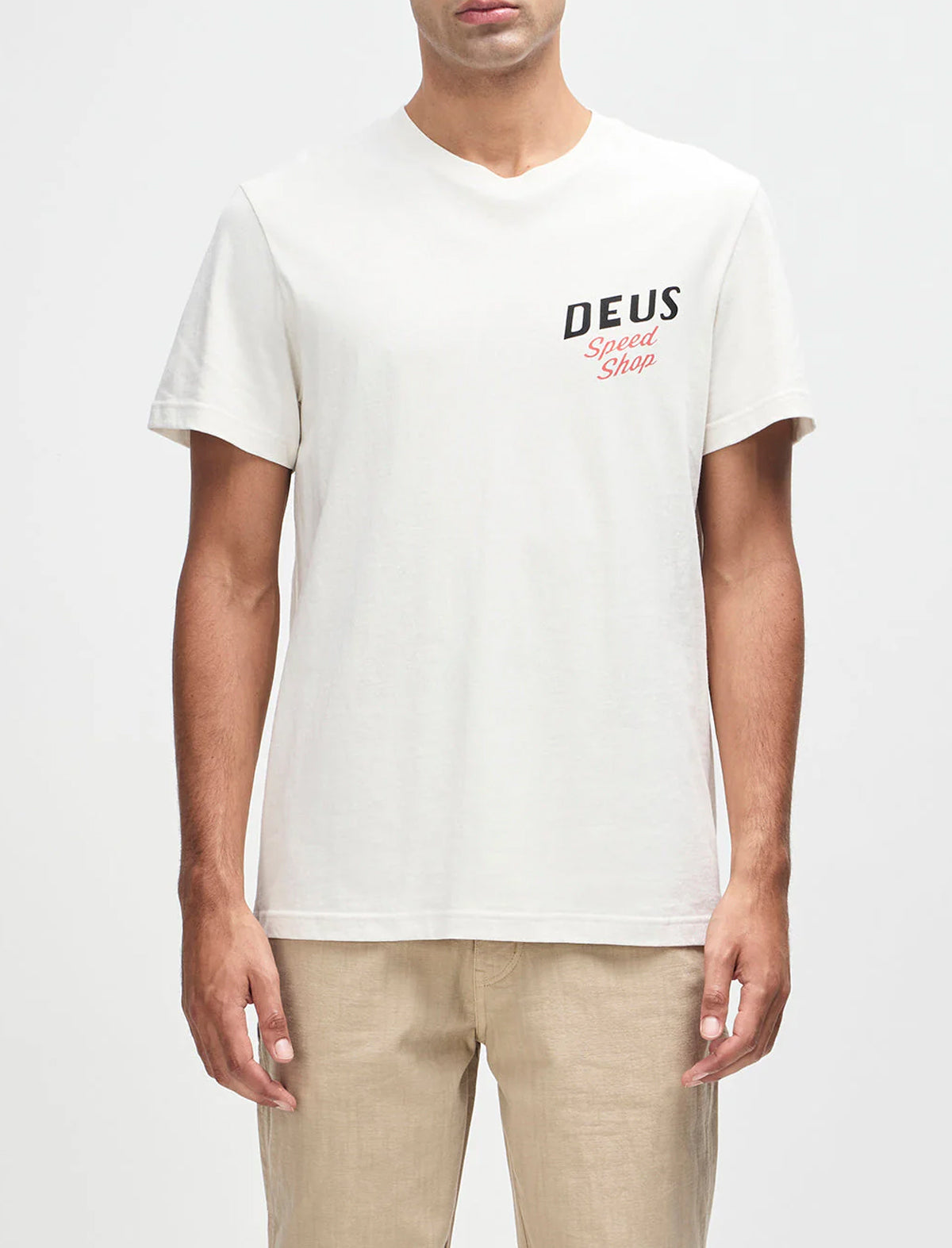 Person wearing a white t-shirt with 'Deus' logo on a plain background