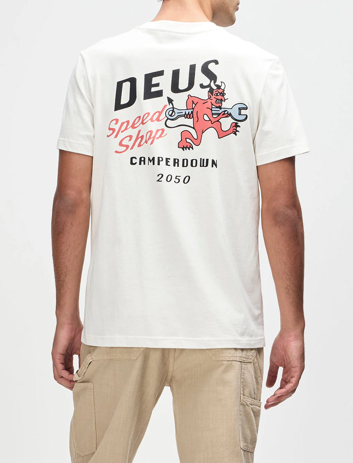 Person wearing a white t-shirt with 'Deus' logo and design on a plain background