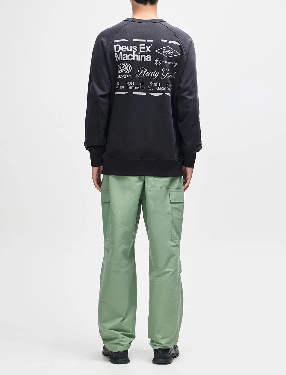 Person wearing a black long-sleeve shirt with text and green pants on a white background