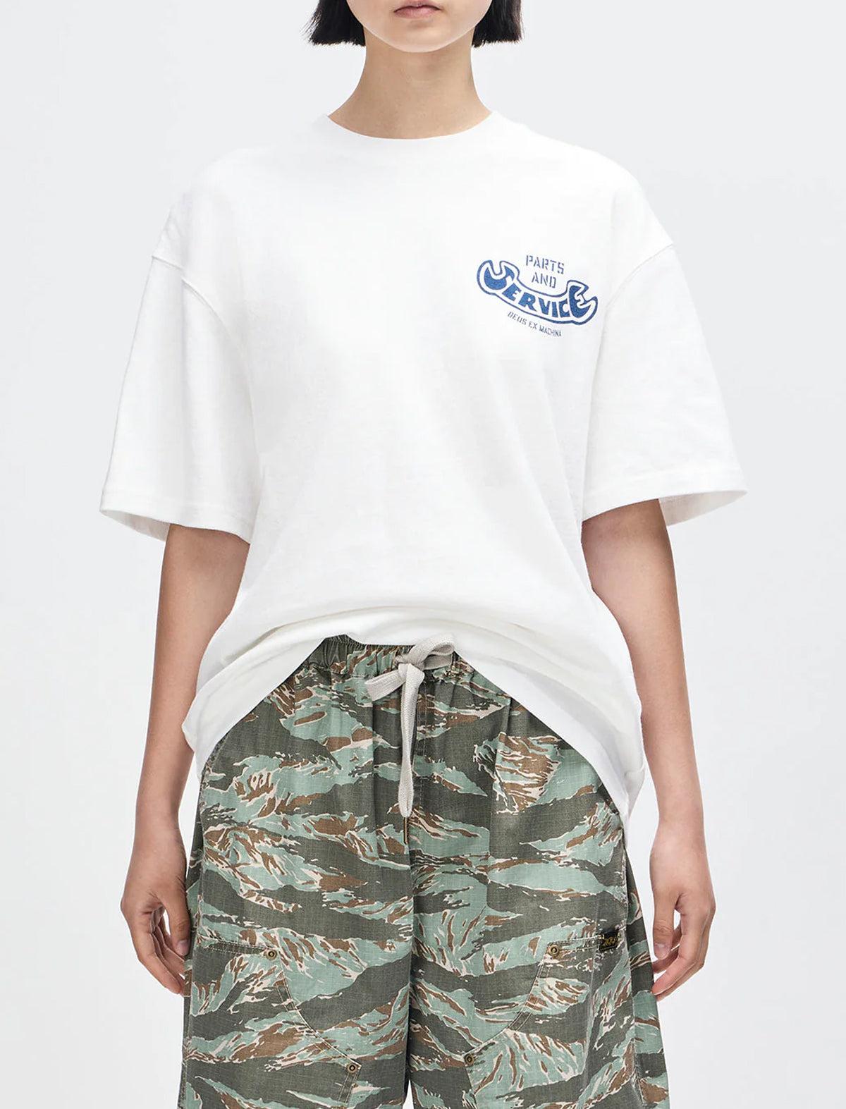 Person wearing a white t-shirt with a logo and camouflage pants on a white background