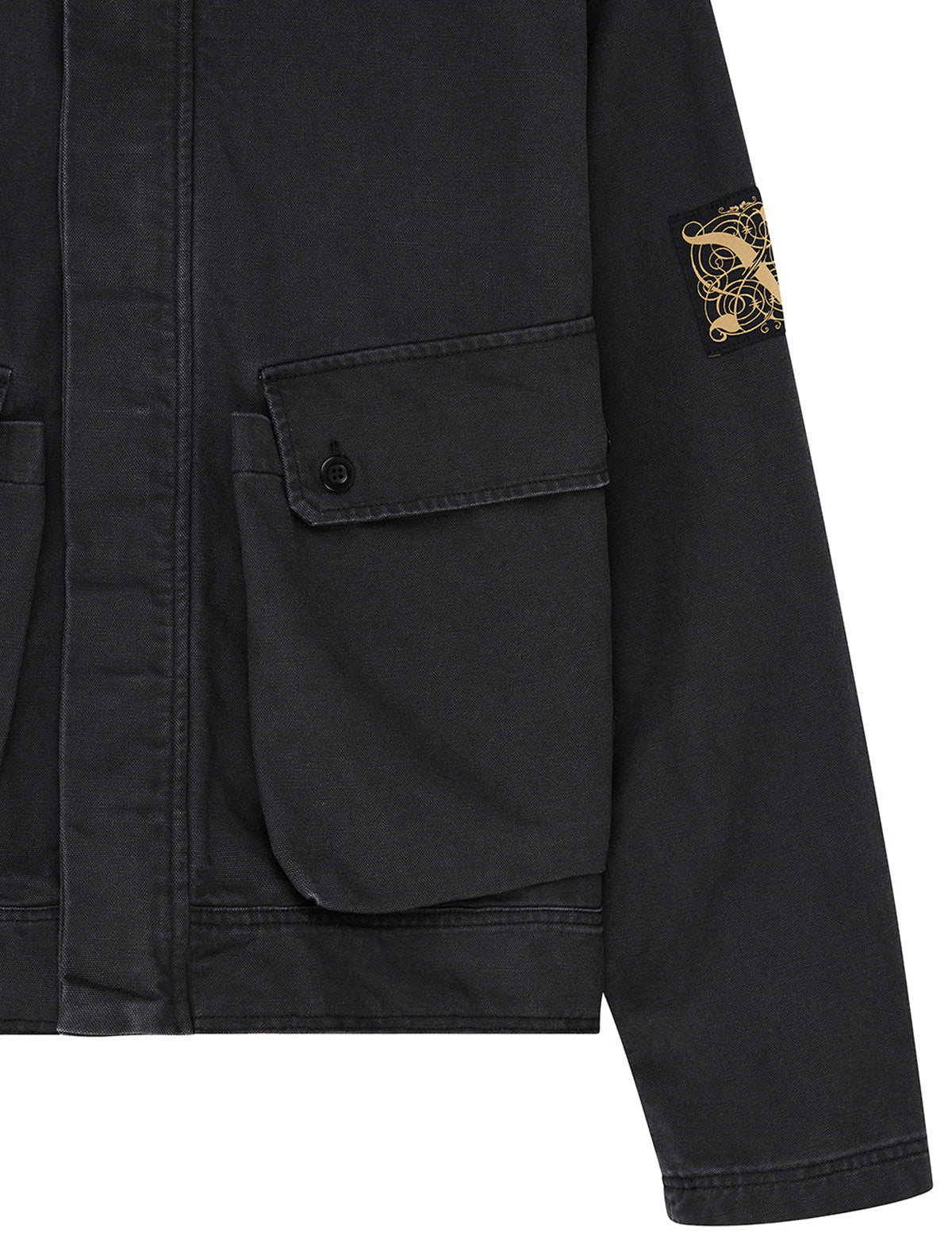 Close-up of a black canvas utility jacket with a flap pocket and a gold-tone Stone Island compass patch on the sleeve, shown against a white background.