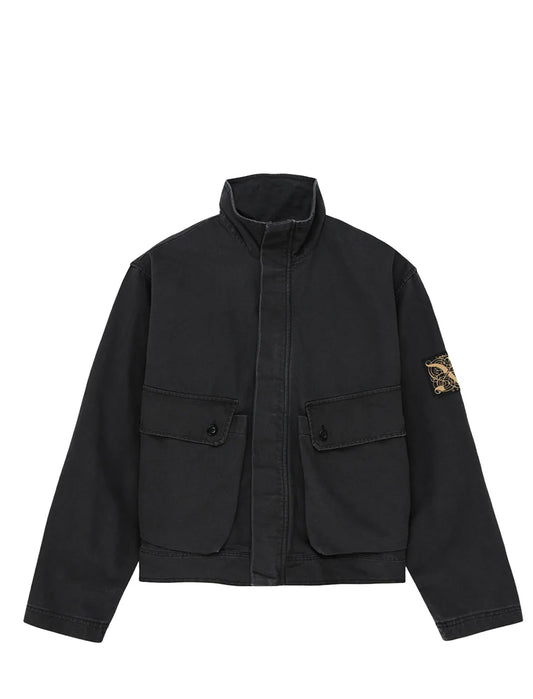 A black Deus Ex Machina utility jacket with a stand collar, front button closure, and two large flap pockets on the chest, featuring the signature Stone Island compass patch on the left sleeve.