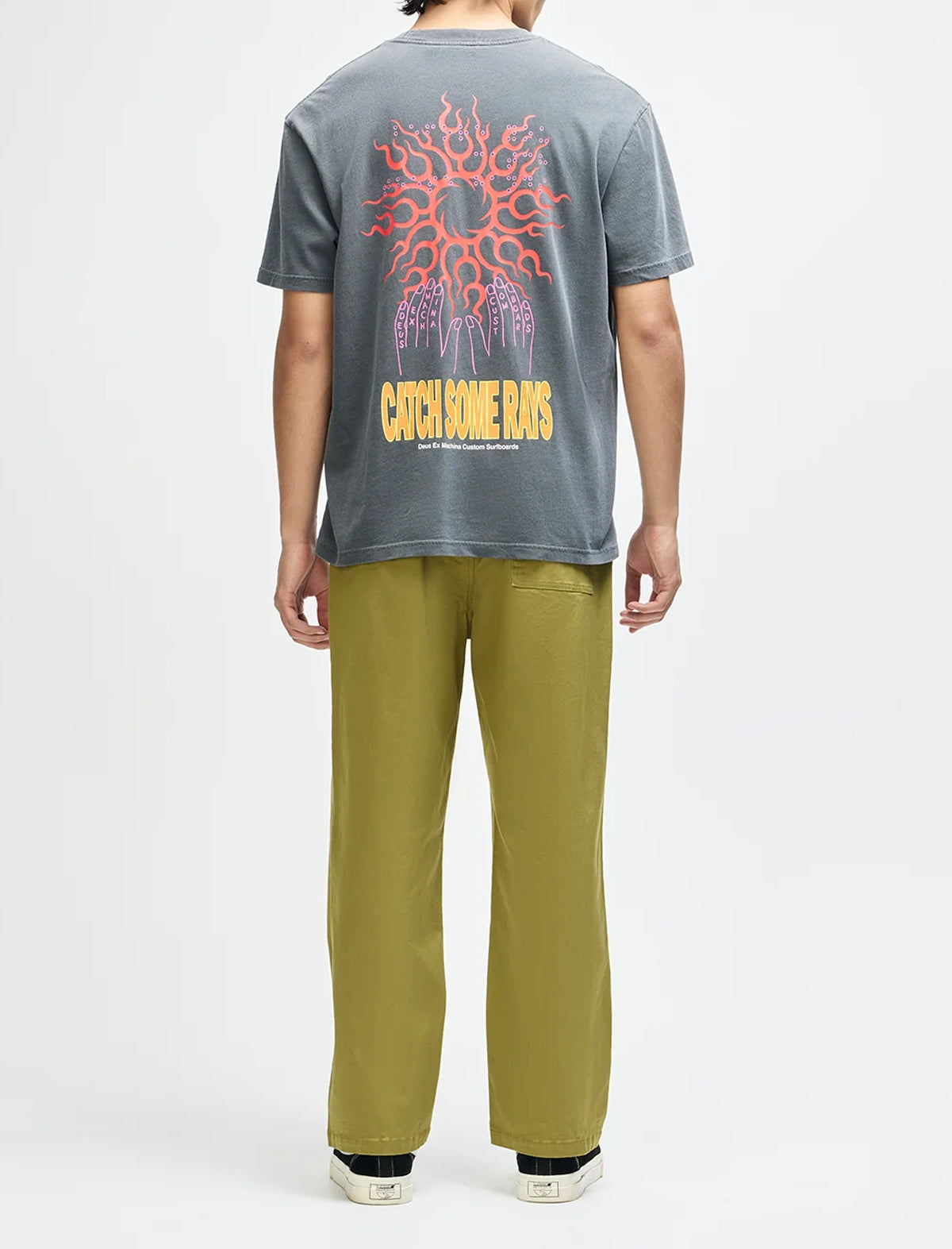A person shown from the back wearing a faded gray t-shirt with a large red and yellow graphic print on the back, paired with olive green pants and black sneakers, against a plain white studio background.