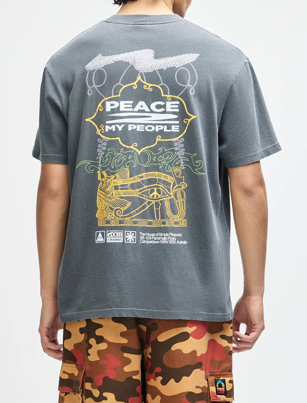 A person shown from the back wearing a faded dark gray t-shirt with a large yellow, white, and green graphic print on the back, paired with camouflage cargo shorts against a plain white background.