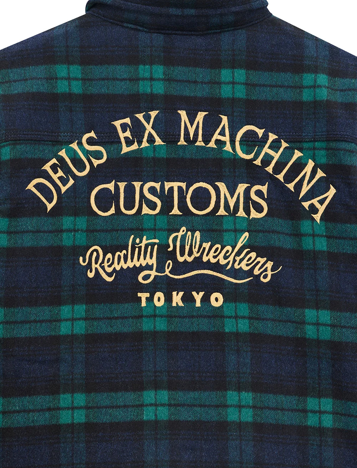 Close-up of the back of a plaid flannel shirt in dark navy and green tartan with large gold embroidered text reading 'DEUS EX MACHINA CUSTOMS Reality Wreckers TOKYO'.