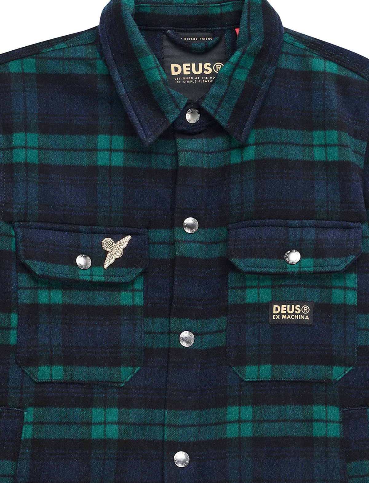 Close-up of a DEUS ex Machina plaid flannel shirt jacket in dark navy and green, featuring silver snap buttons, a wing pin, and a chest patch.