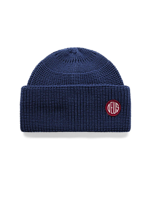 A navy blue ribbed knit beanie hat with a small circular embroidered logo on the front cuff. The logo is red with white lettering that reads 'DELG'.