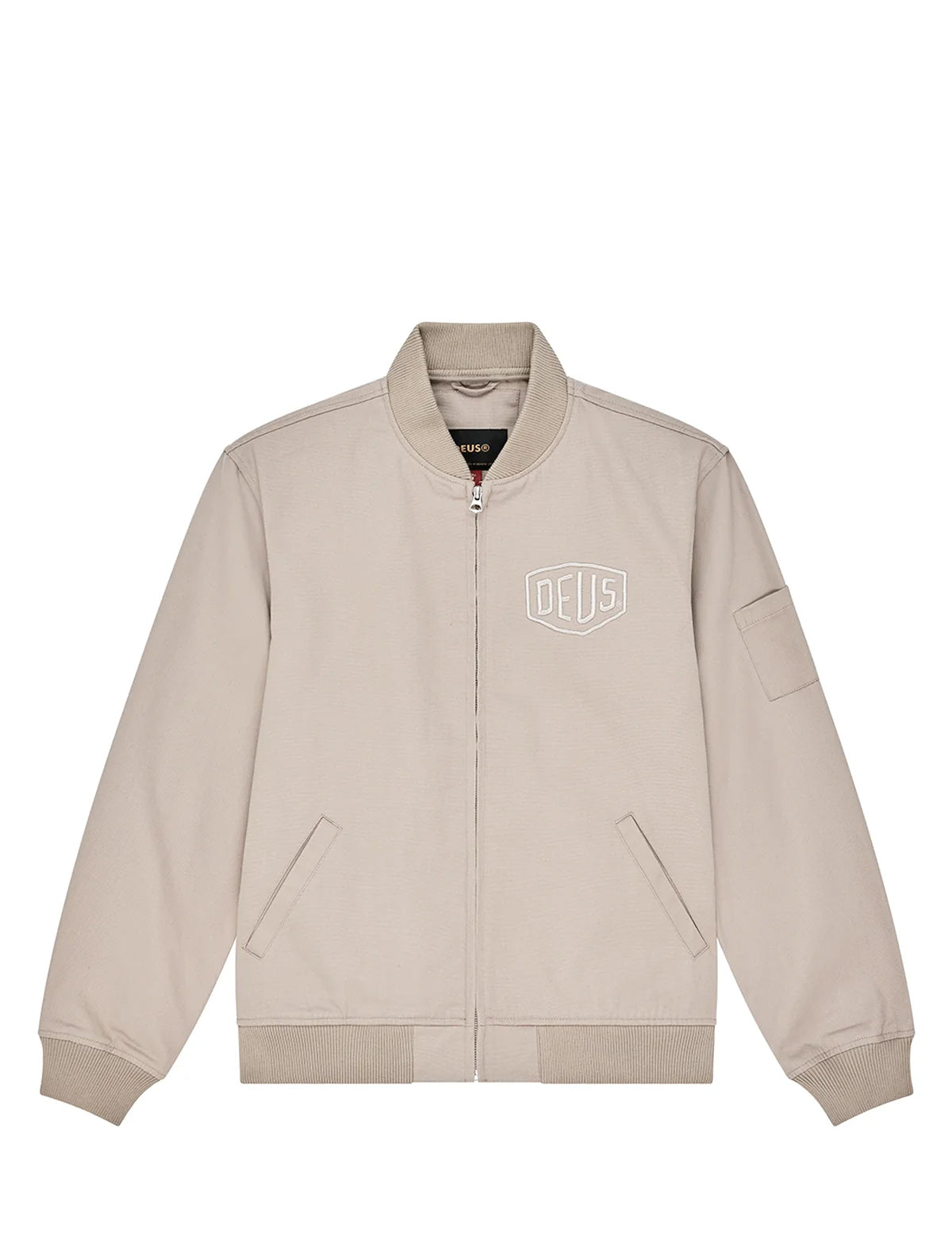 A light beige zip-up bomber jacket with a white outlined 'DEUS' shield logo on the left chest, displayed flat against a solid white background.