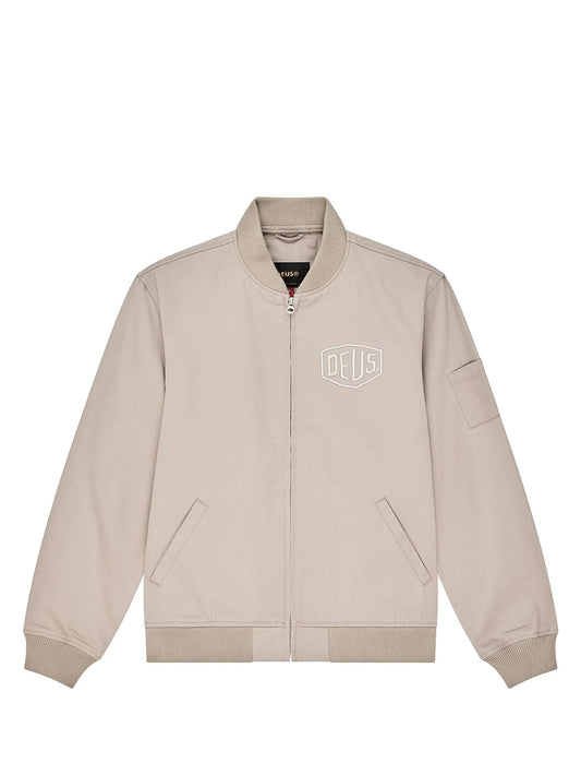 A light beige zip-up bomber jacket with a white outlined 'DEUS' shield logo on the left chest, displayed flat against a solid white background.