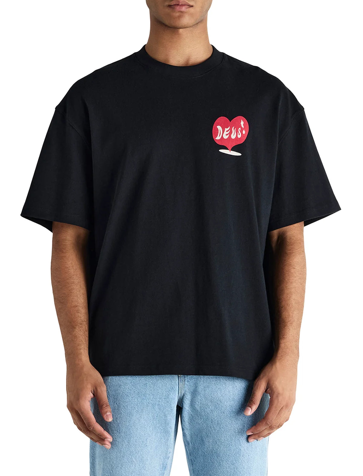 A man wearing a black oversized crewneck t-shirt with a red heart graphic on the left chest that says 'DEUS', paired with light blue jeans, against a plain white background.