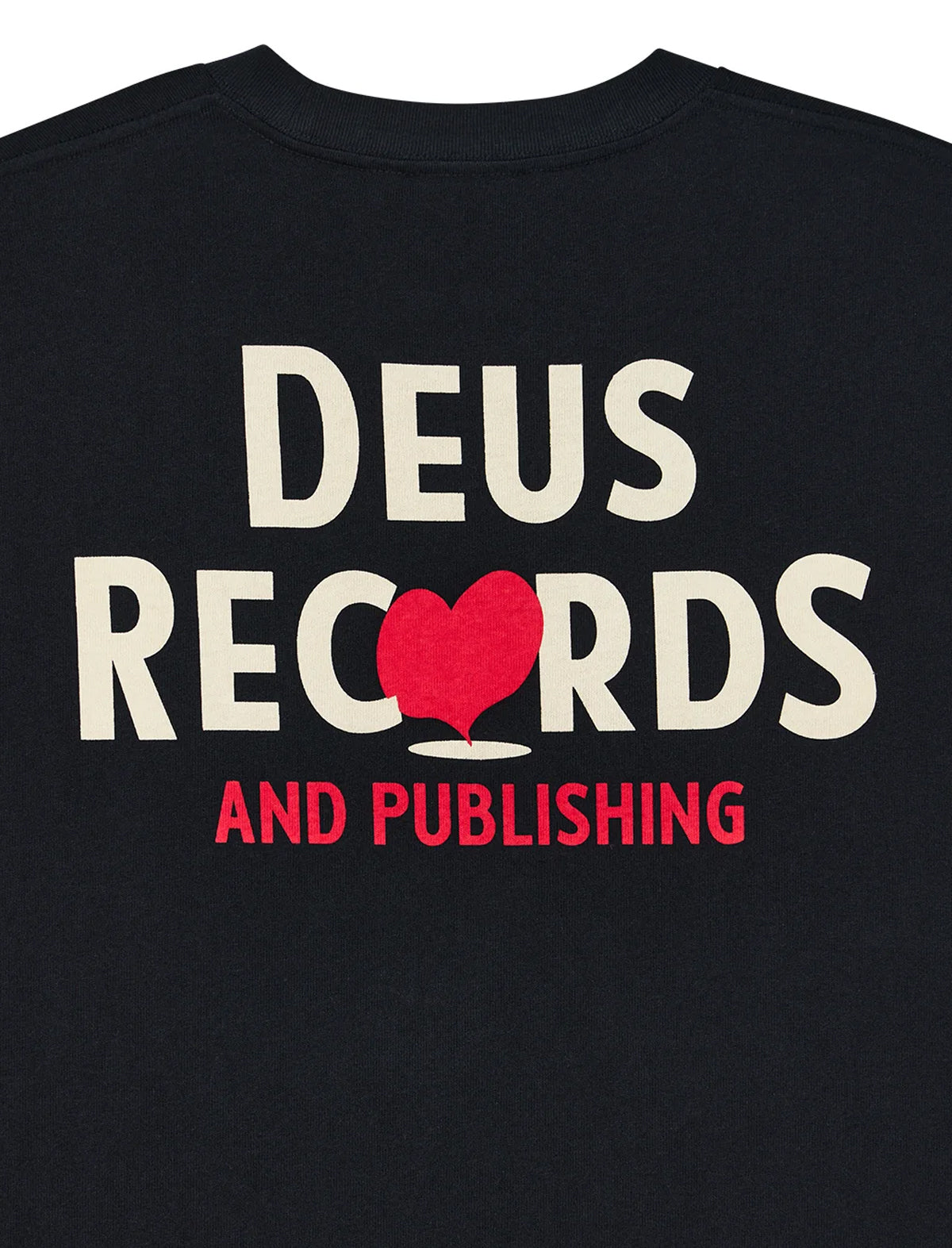 Close-up of a black t-shirt featuring a graphic print with the words 'DEUS RECORDS AND PUBLISHING'. The letter 'O' in 'RECORDS' is replaced by a red heart playing card symbol, and 'AND PUBLISHING' is printed in red below.