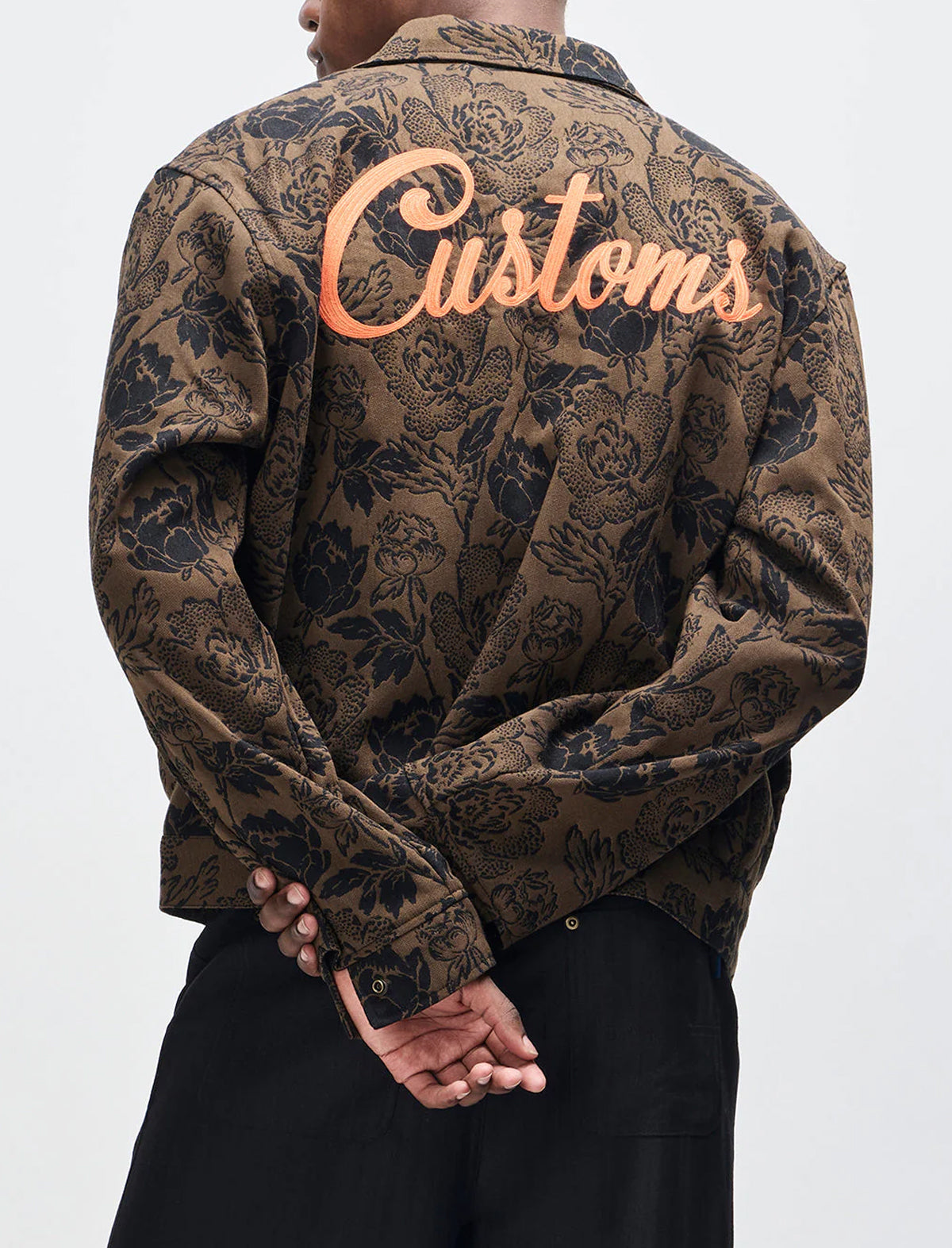 Person wearing a patterned jacket with 'Customs' text on the back against a white background