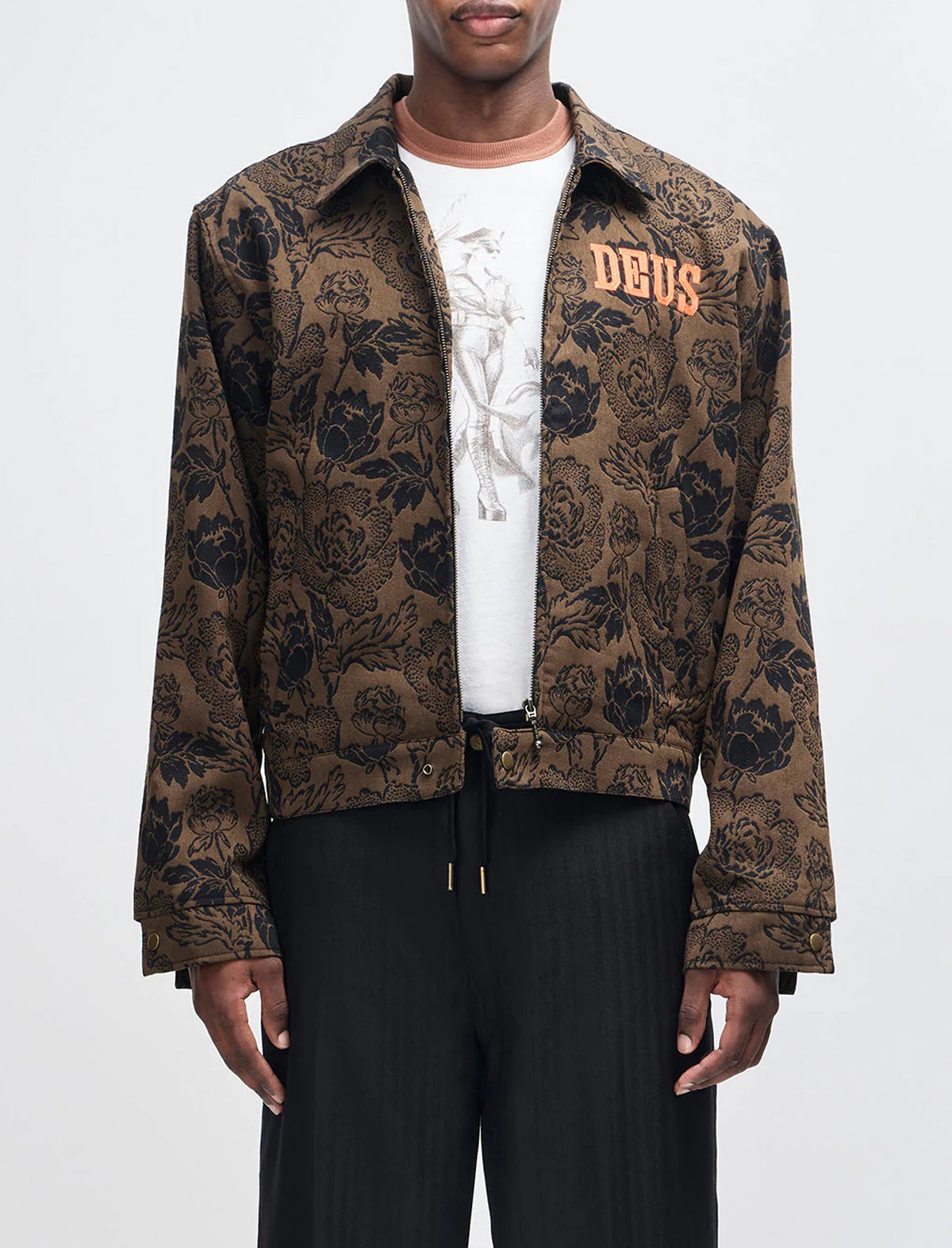 Man wearing a patterned jacket with 'DEUS' branding on a white background