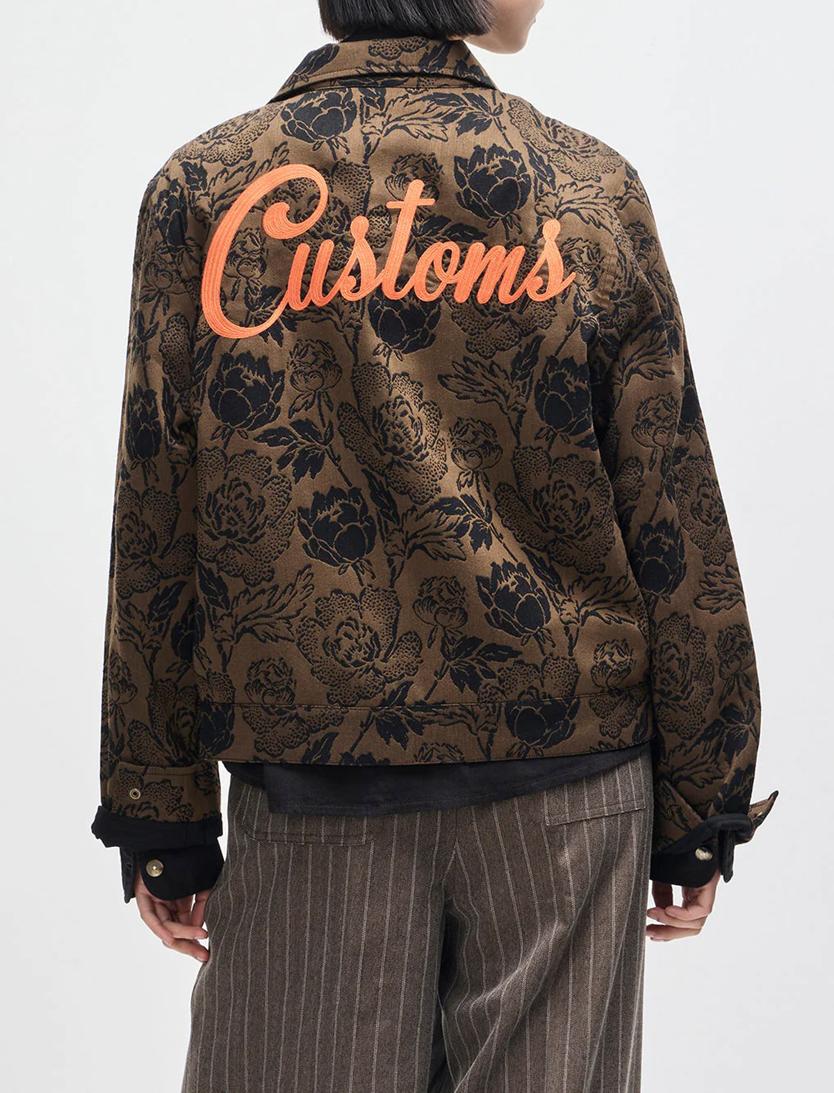 Floral patterned jacket with 'Customs' text on the back, worn by a person.