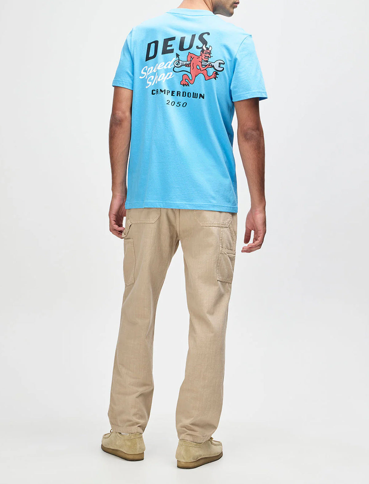 Person wearing a blue t-shirt with a logo and text, standing against a white background