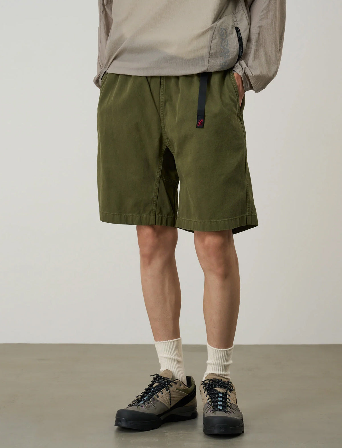 Person wearing green shorts, beige jacket, and hiking shoes on a plain background