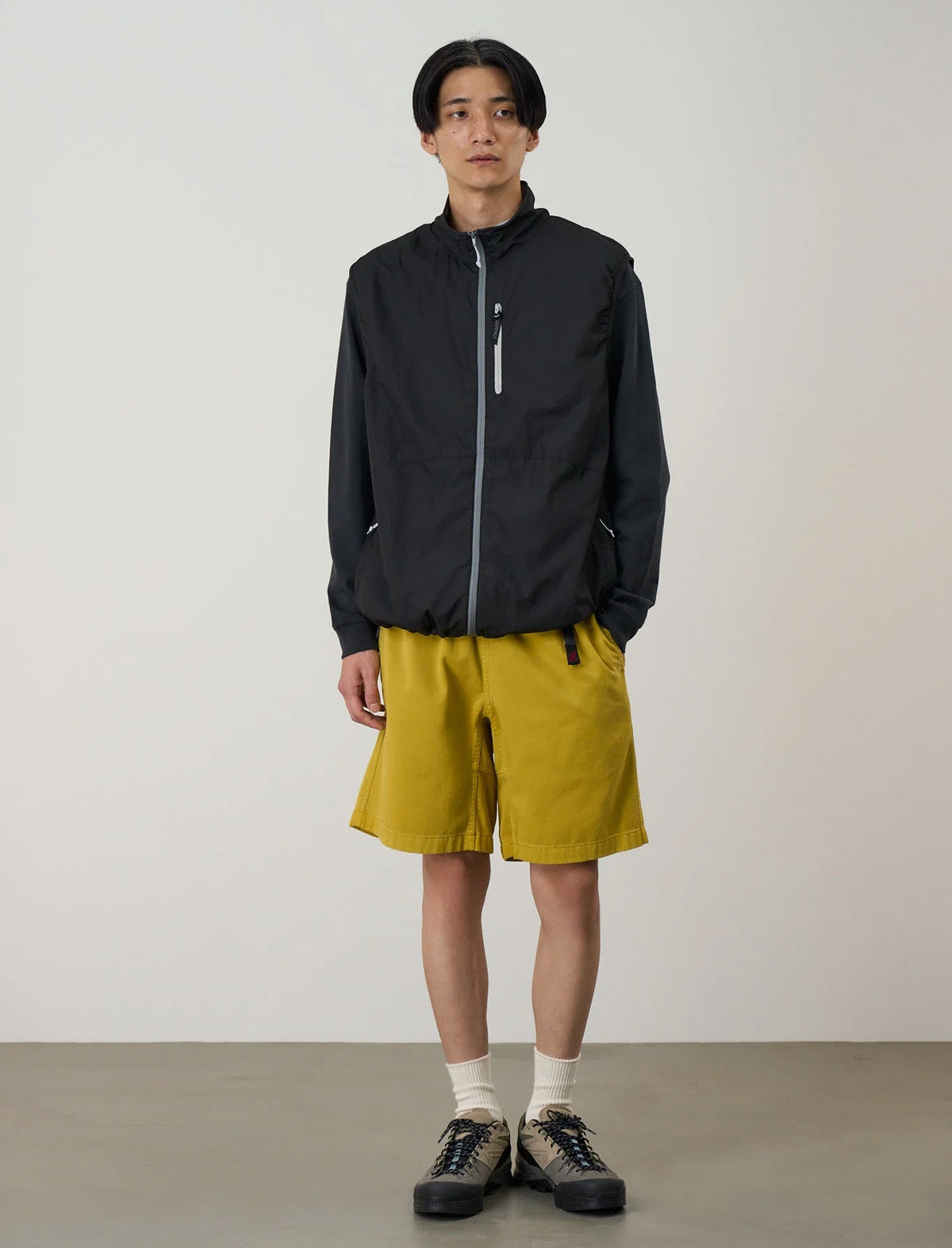 Person wearing a black jacket and mustard yellow shorts against a plain background