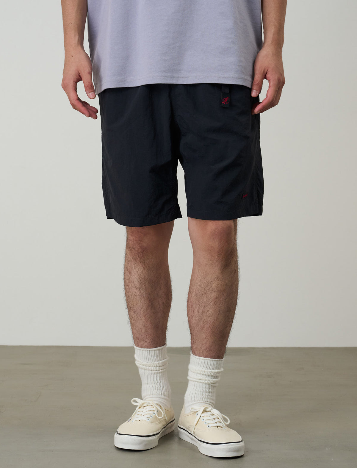 Person wearing black shorts, white socks, and white sneakers on a plain background
