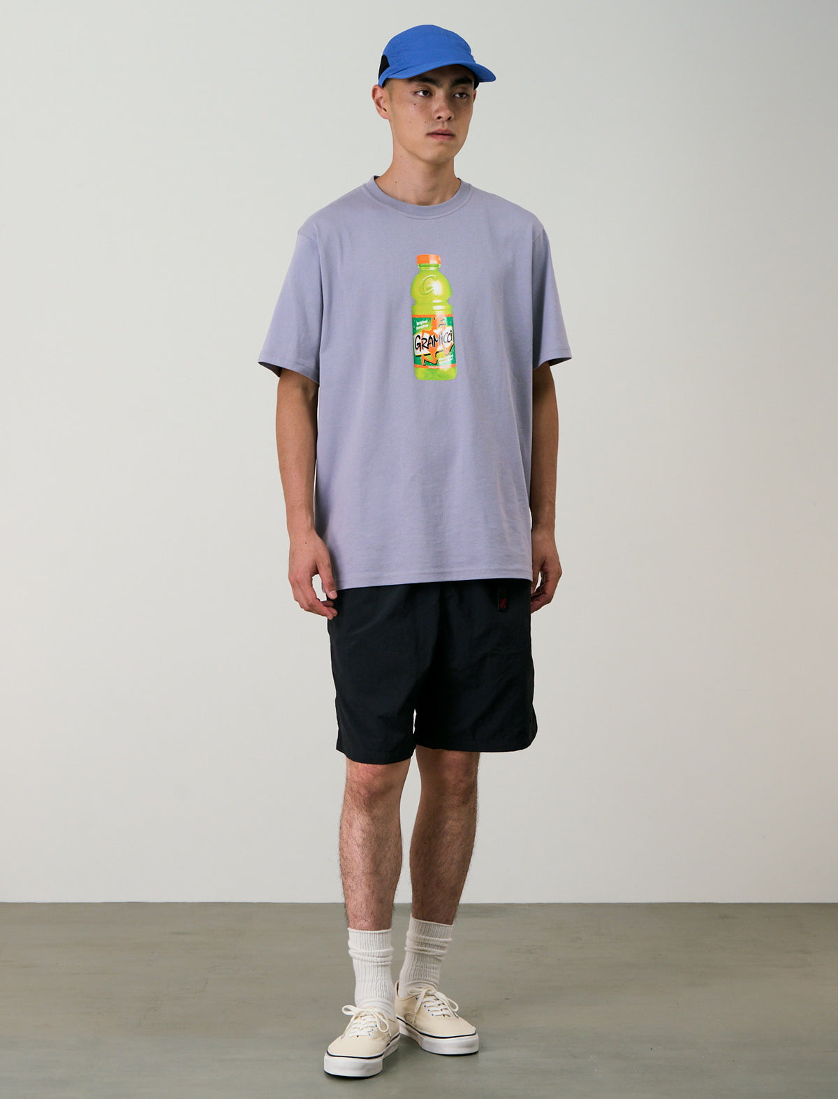 Person wearing a light purple t-shirt with a bottle graphic and black shorts against a plain background